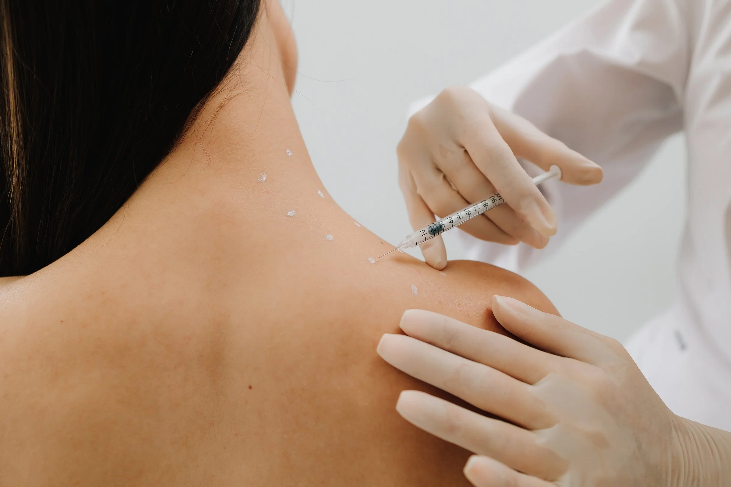An osteopathic physician administering an injection into a woman's upper arm. The woman has dark hair and appears to be receiving the shot in a clinical setting.