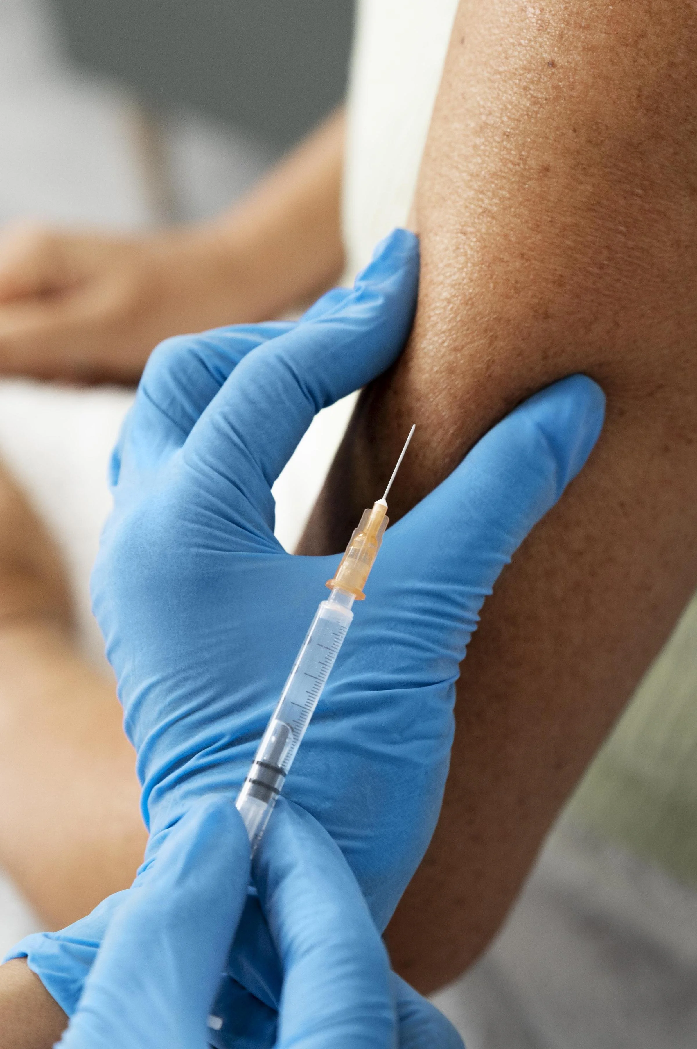 A person wearing blue gloves injecting into a person's upper arm.