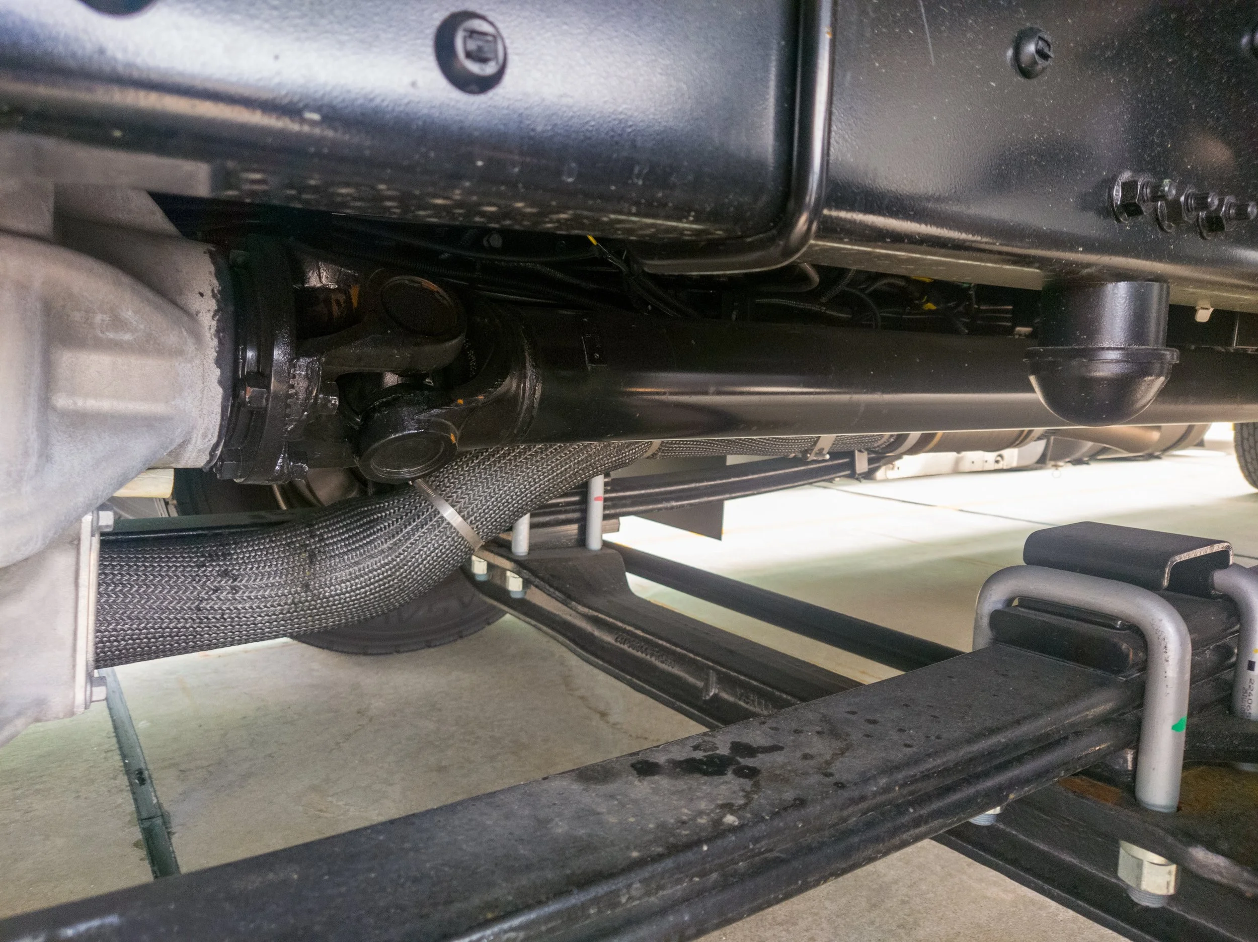 Underneath a vehicle, showing parts of the car's suspension, wiring, and a black support or frame. The image appears to have been taken in a garage or workshop setting.