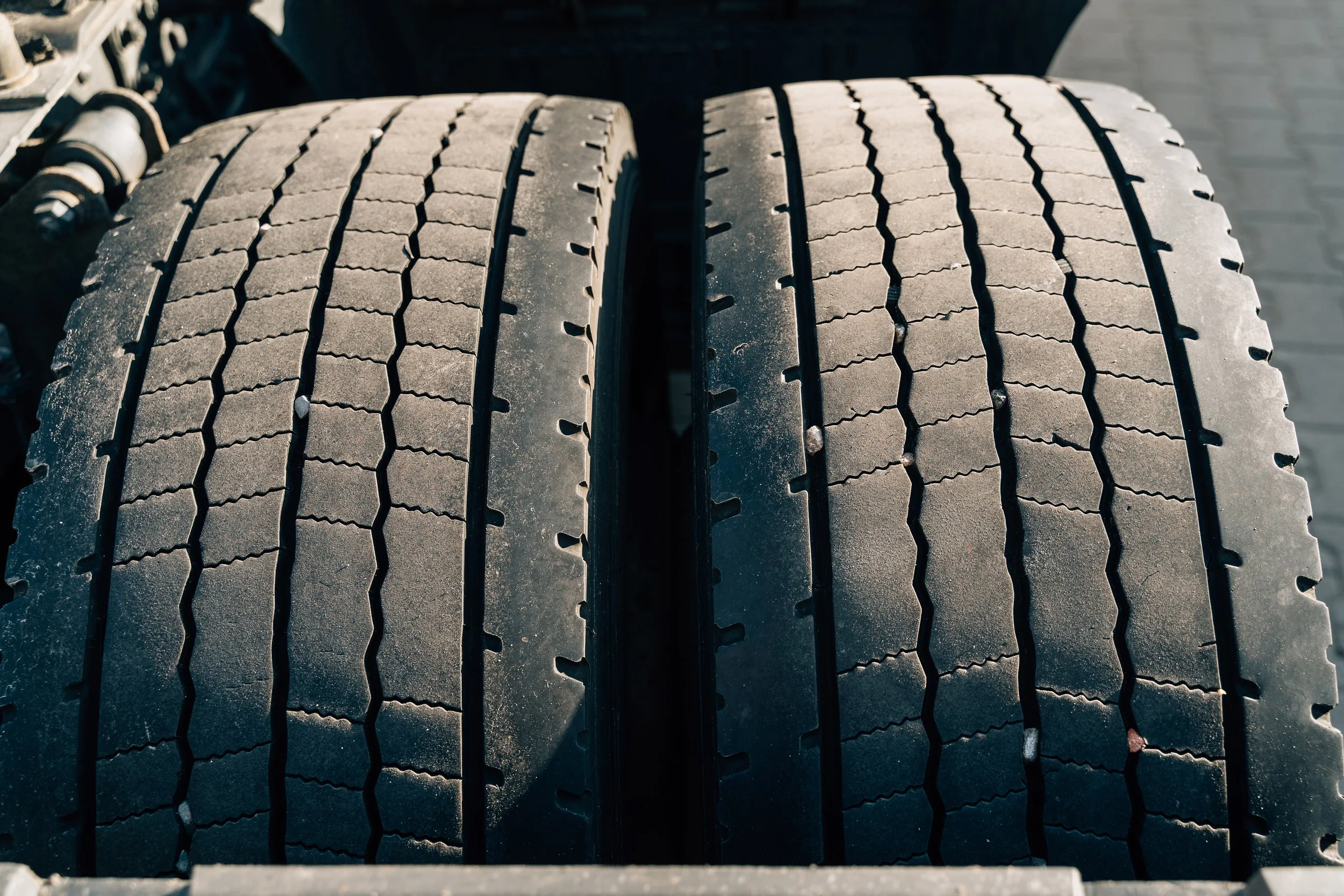 Close-up of two black truck tires with visible tread pattern, mounted on a vehicle, side view