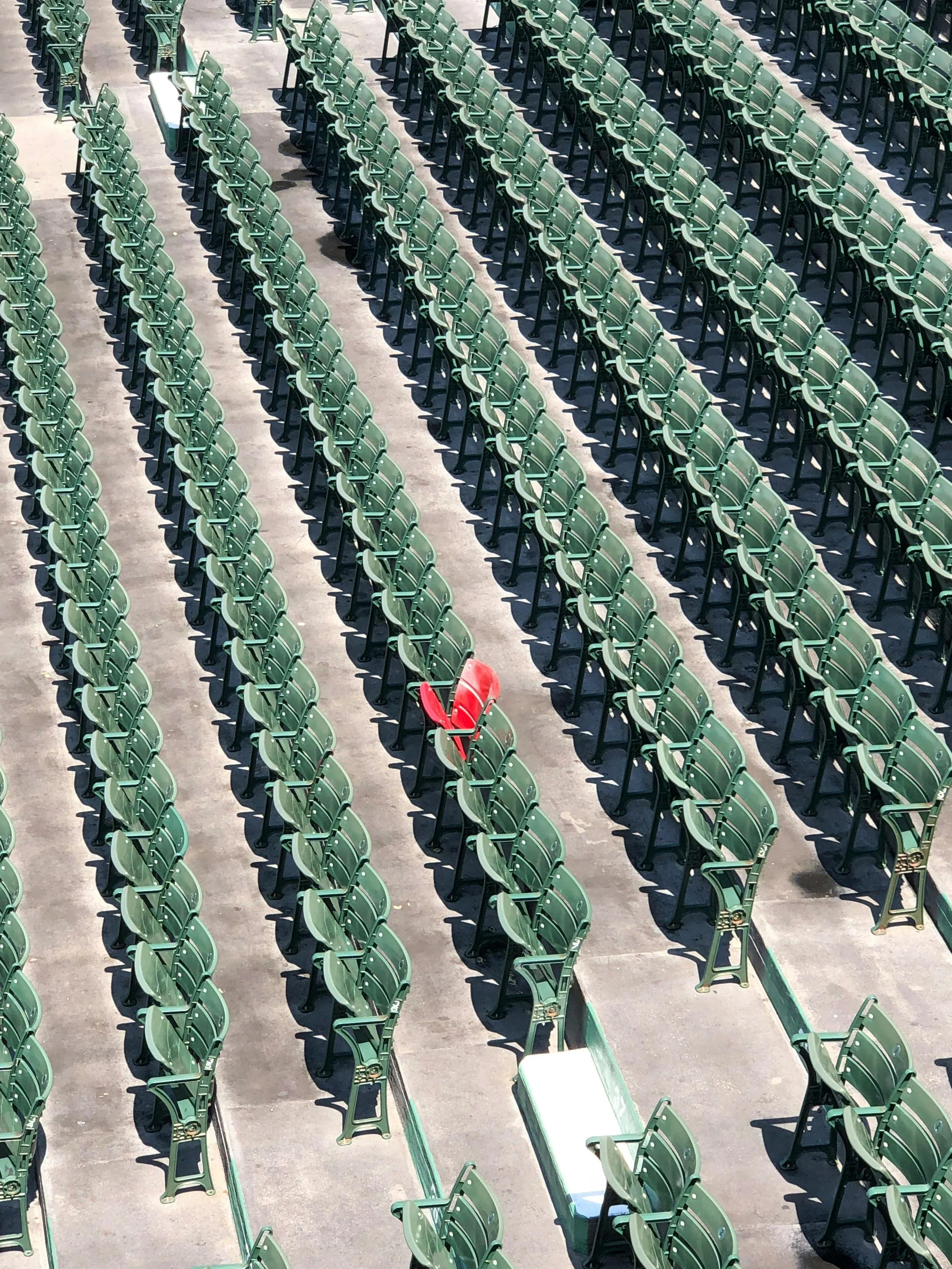 Numerous green chairs arranged in rows on a concrete surface, with a single red chair among them.