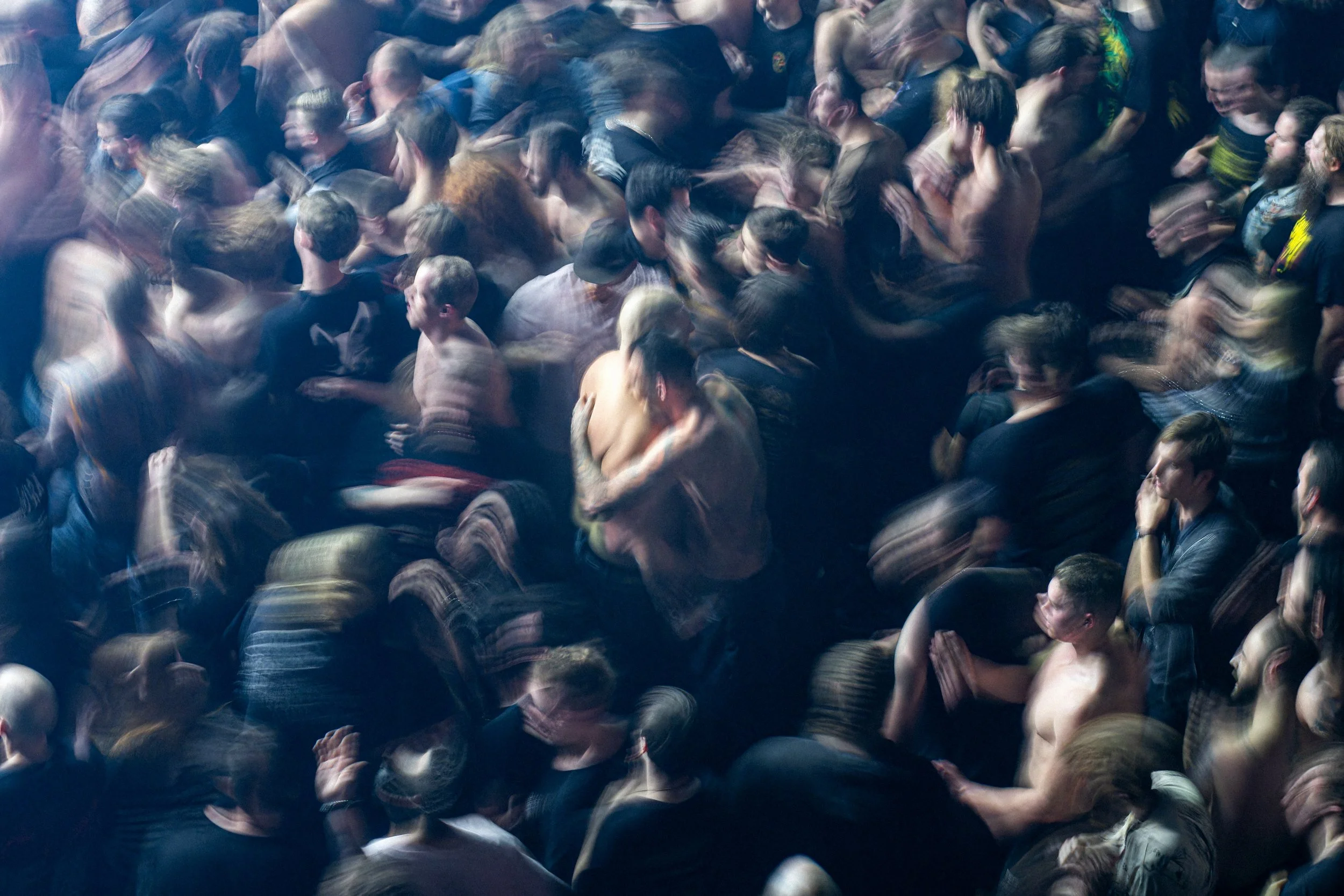 A crowd of people tightly packed together, some appear to be moving or dancing, creating a blurry effect.