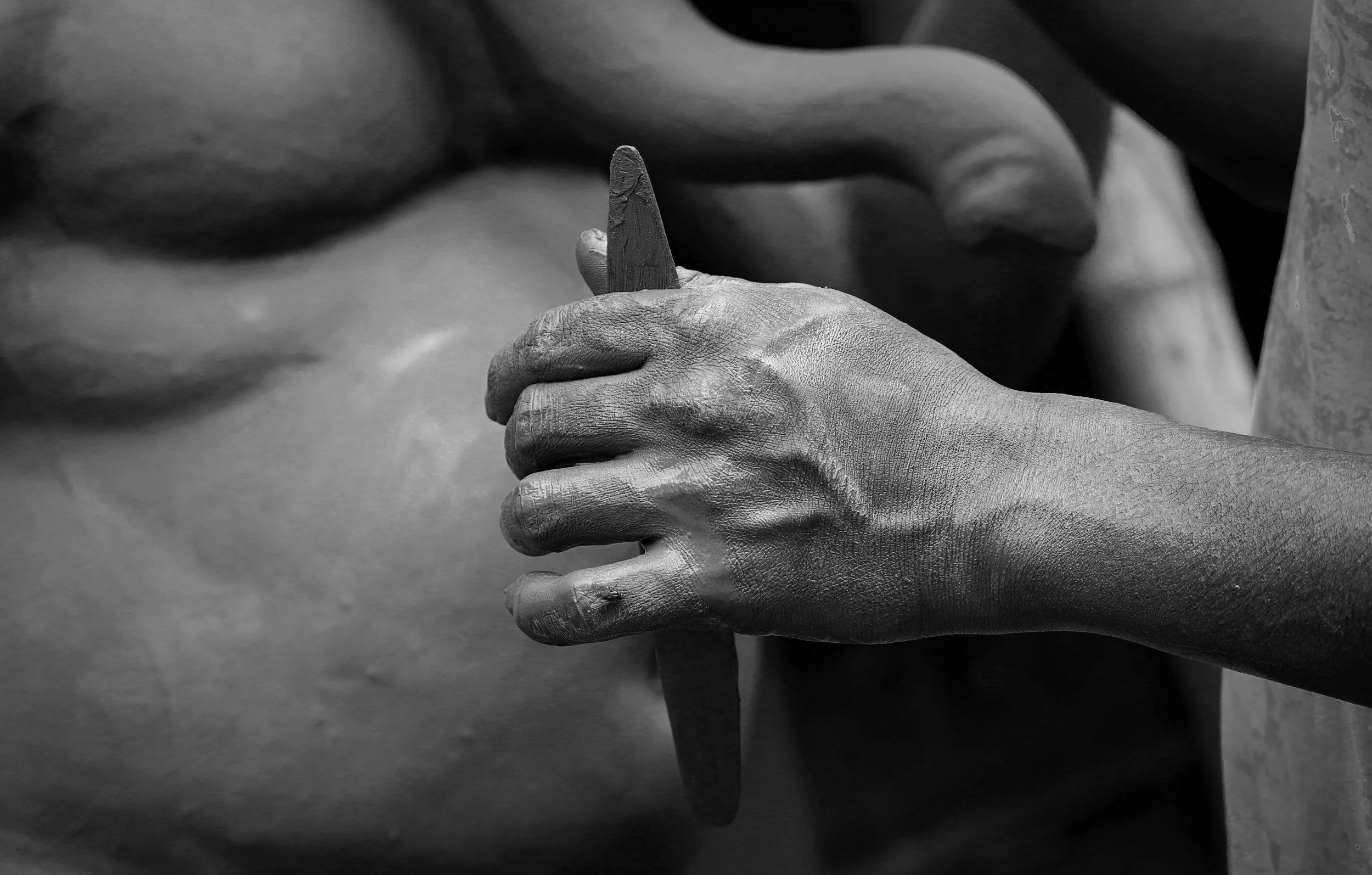 Close-up black and white image of a person shaping a sculpture with their hand, focusing on the hand and the sculpture's head.