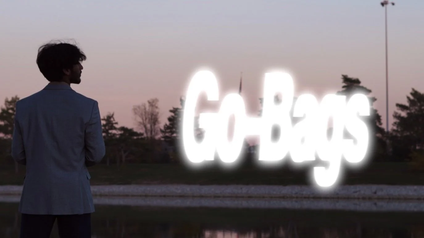A man in a blazer stands outdoors at sunset, looking at a neon sign that says 'GOBIS' with some trees and streetlights in the background.