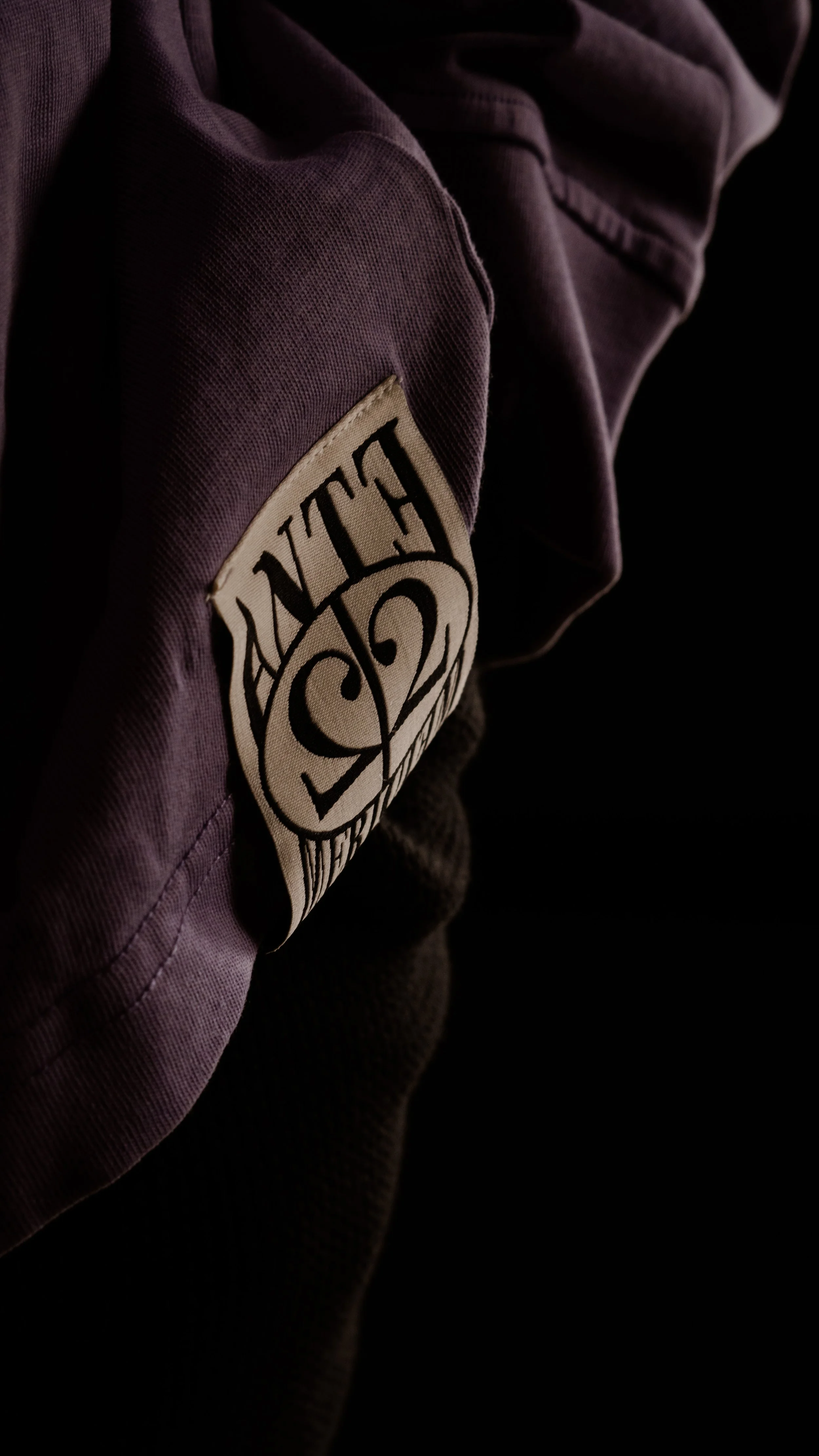 A close-up of a purple jacket with a circular patch that has black text on a white background, showing the word 'CULTURE' upside down.