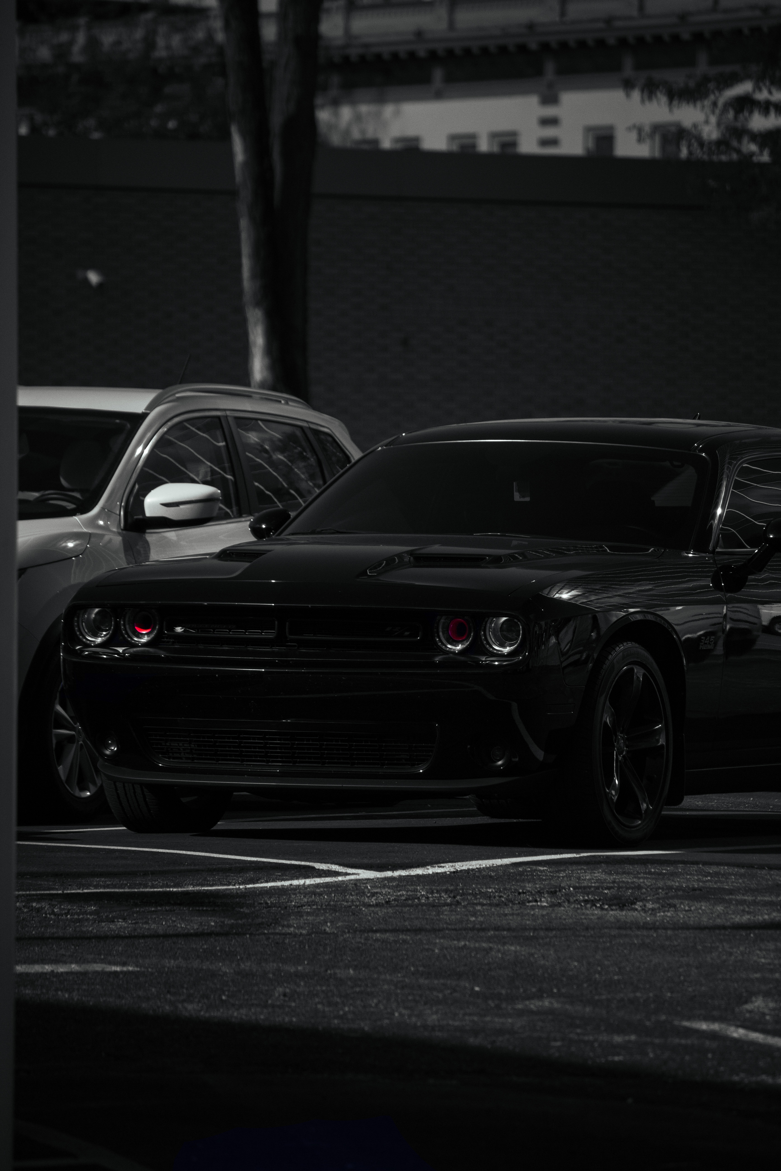 A black Dodge Charger parked in a parking lot with a white car nearby, in a dimly lit outdoor setting at night.