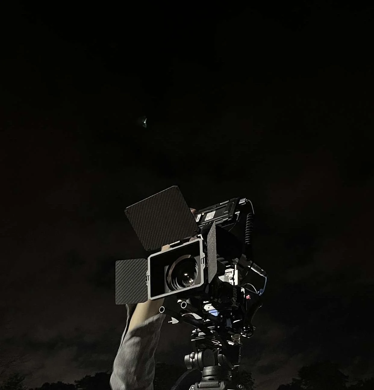 A precision camera mounted on a tripod, being manually adjusted in the dark, with the night sky in the background.