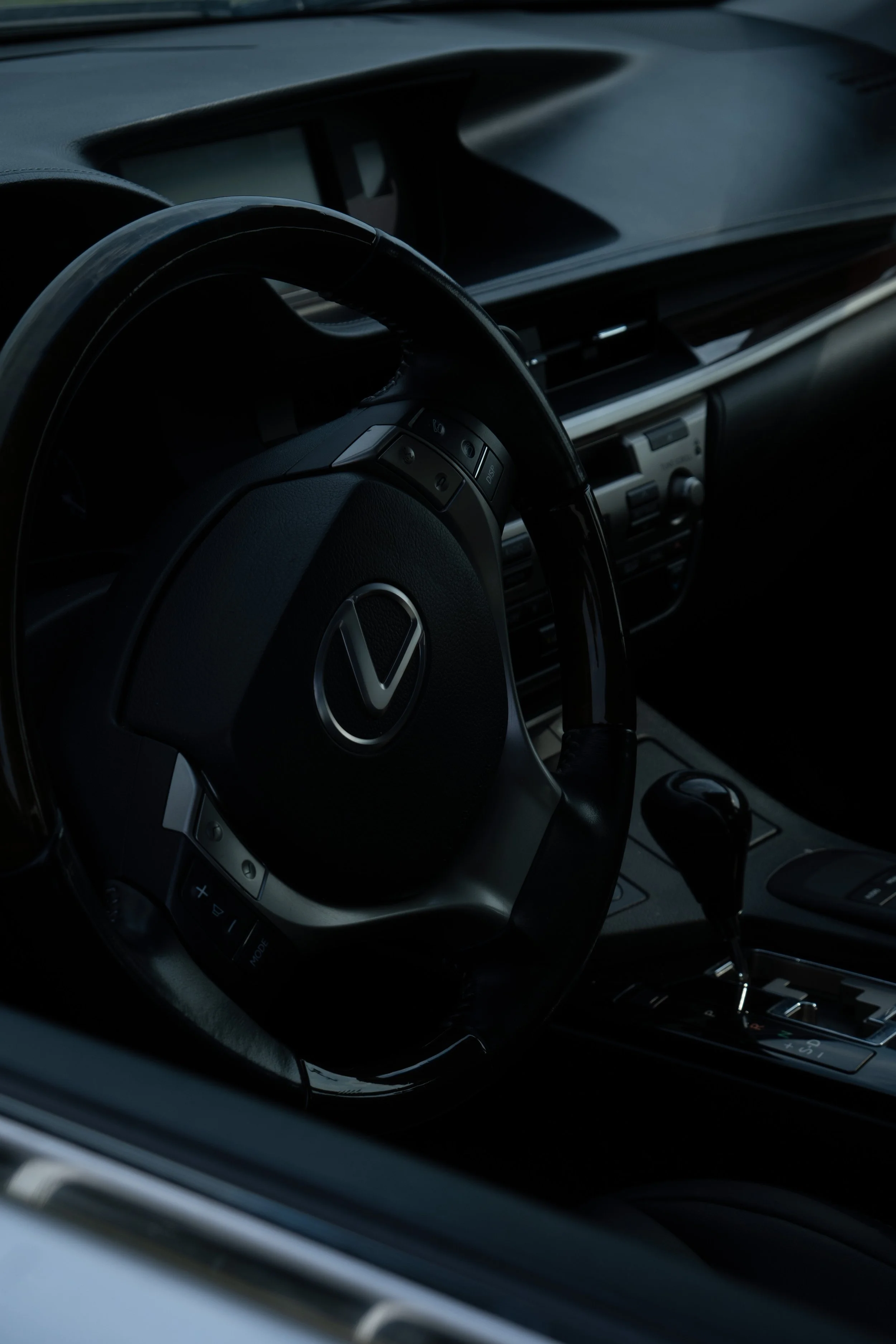 Close-up of a car interior, showing a steering wheel with a logo, dashboard, and gear shift lever.
