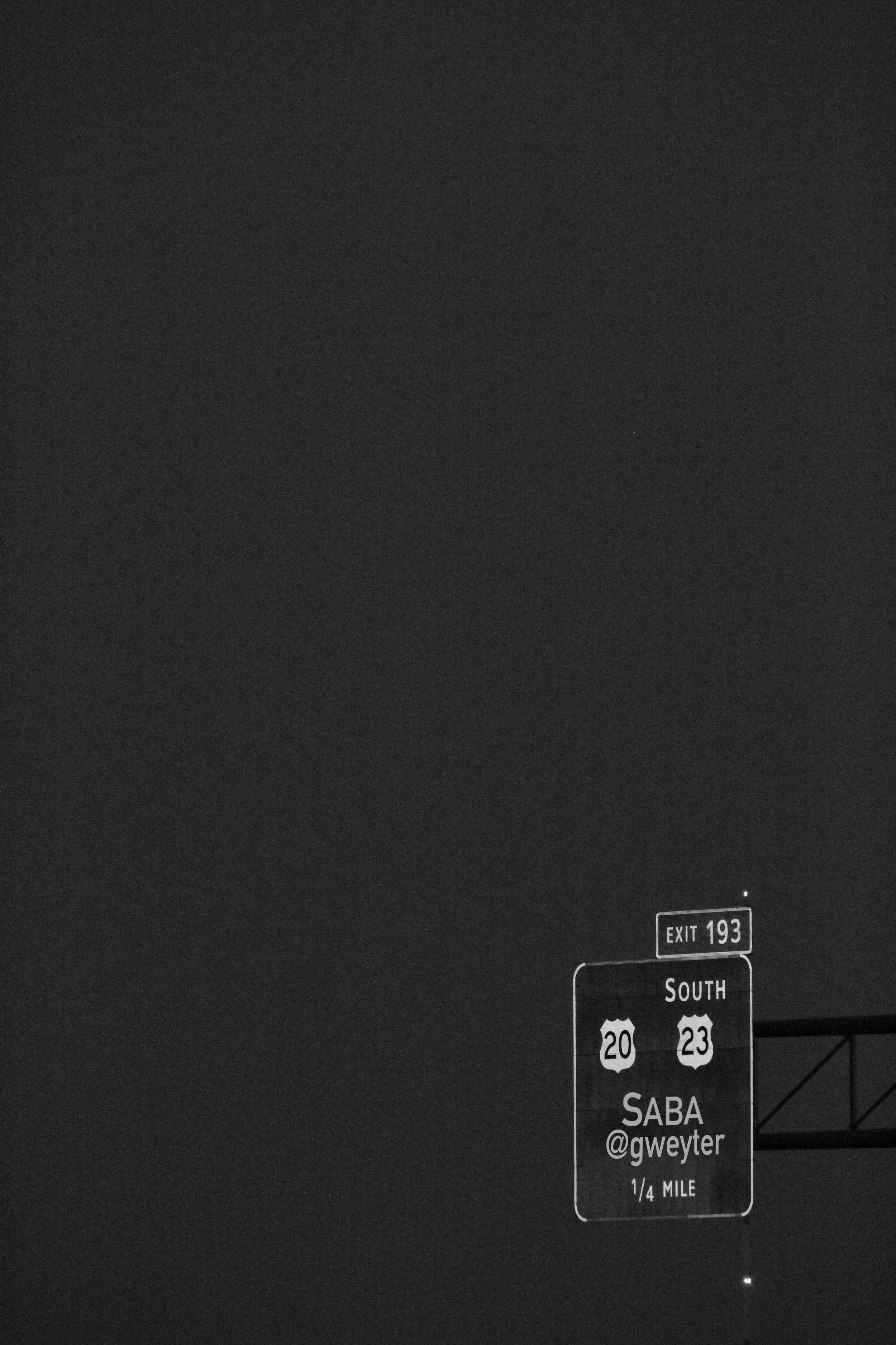 Nighttime highway exit sign indicating Southbound routes for U.S. Highway 20 and 23, with intermediate location SABA and a Twitter handle @gweyter, 1/4 mile ahead.