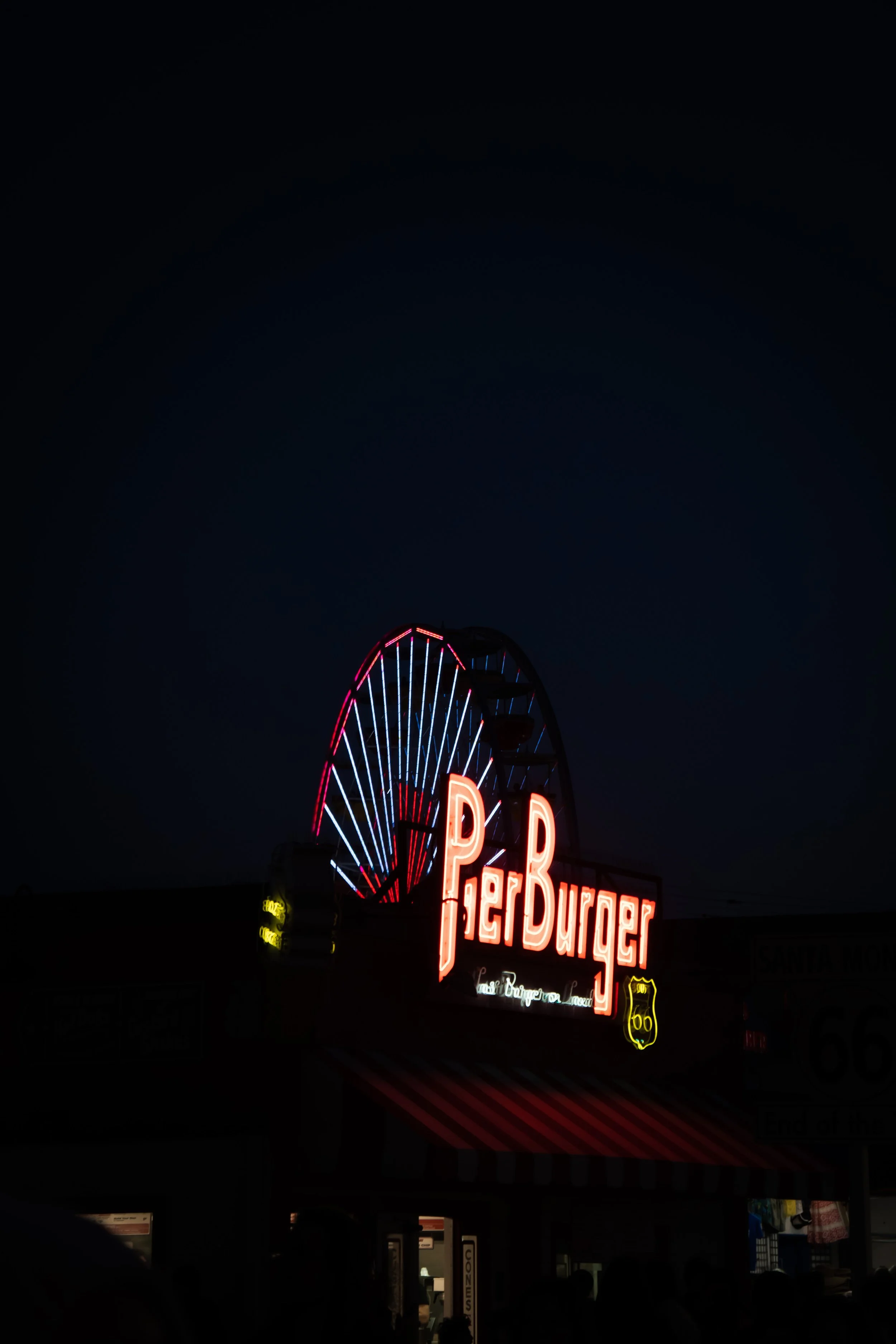 Nighttime neon sign for a P. & B.urger restaurant with a Ferris wheel in the background.