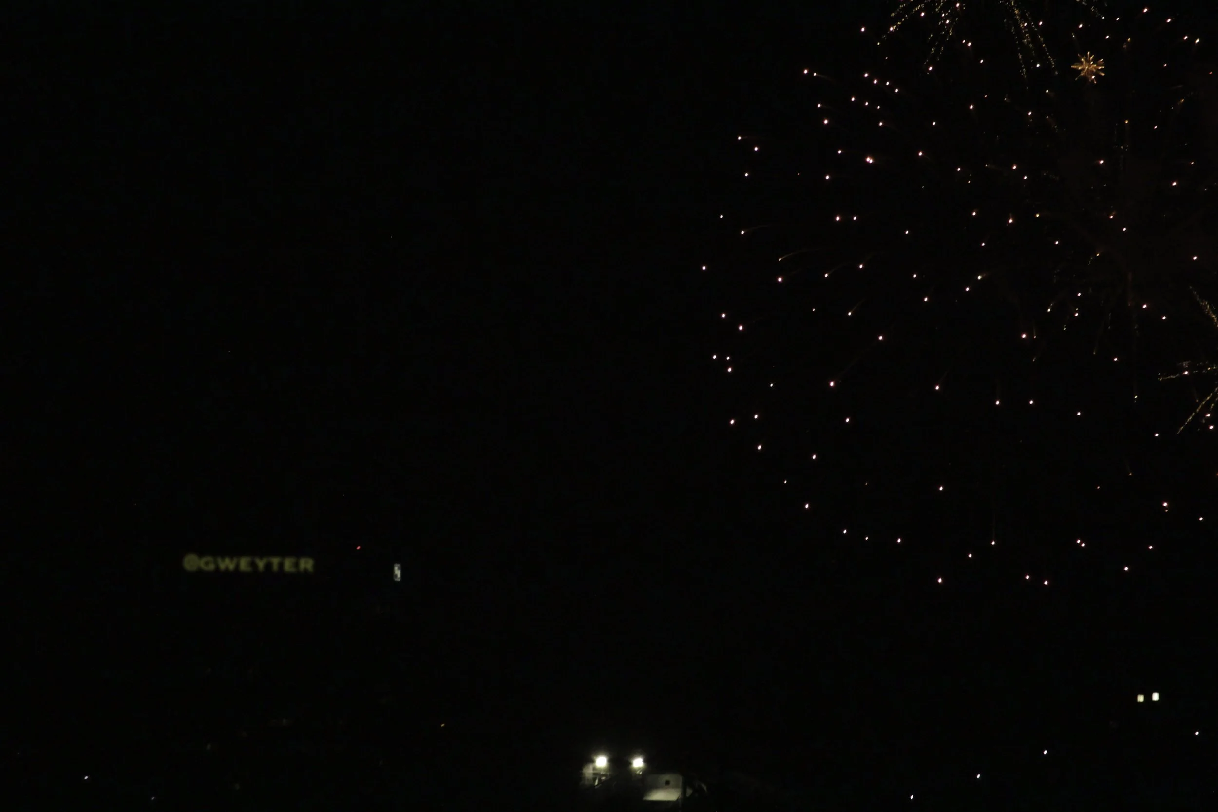Night sky with fireworks and a faint yellow sign reading '@GWEYTER'.