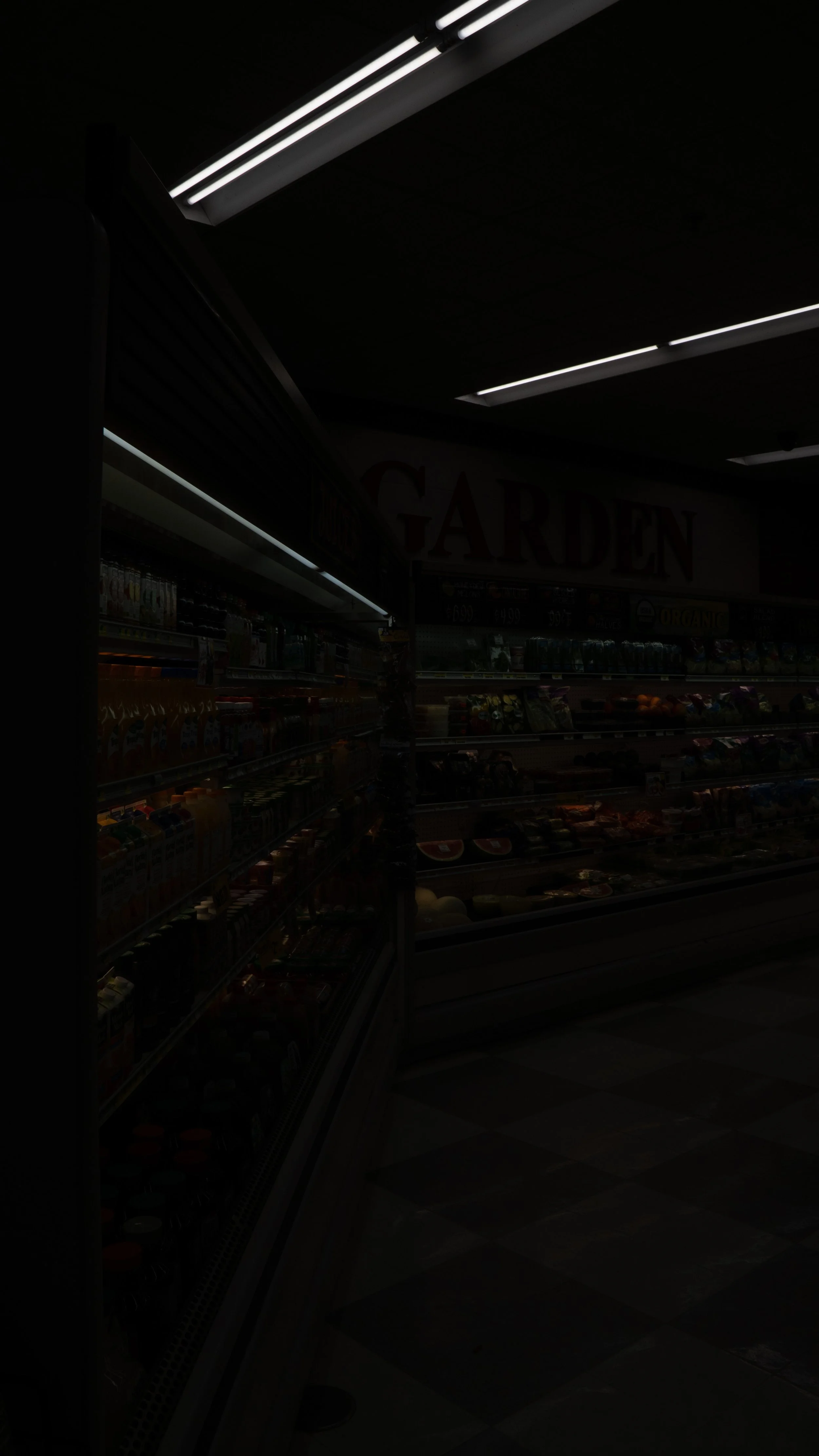 Inside a grocery store with fluorescent lighting and shelves stocked with various products, including beverages and produce, near a sign that reads 'GARDEN'.