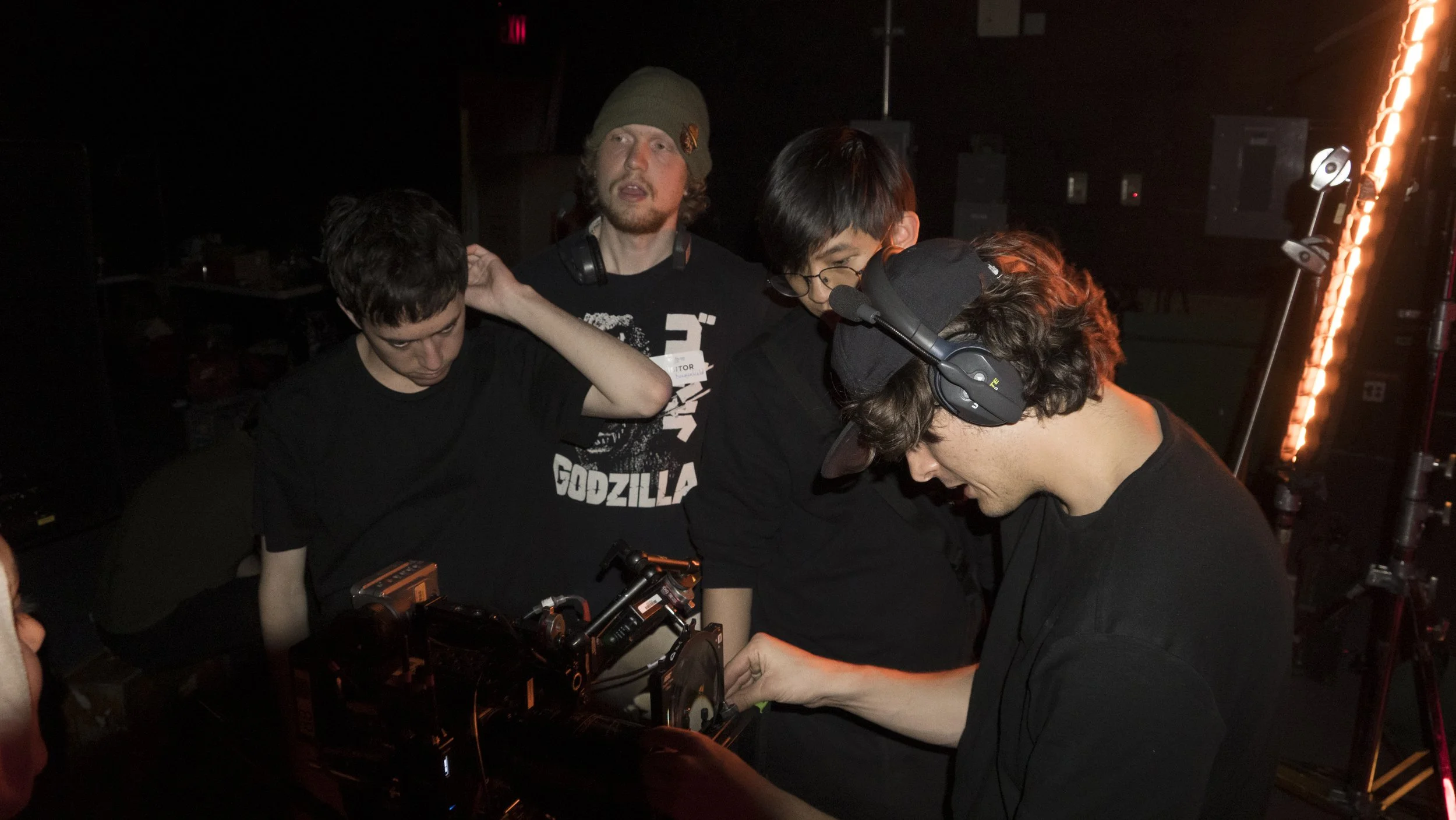Group of young men working on a camera or filming equipment in a dark room with stage lighting.