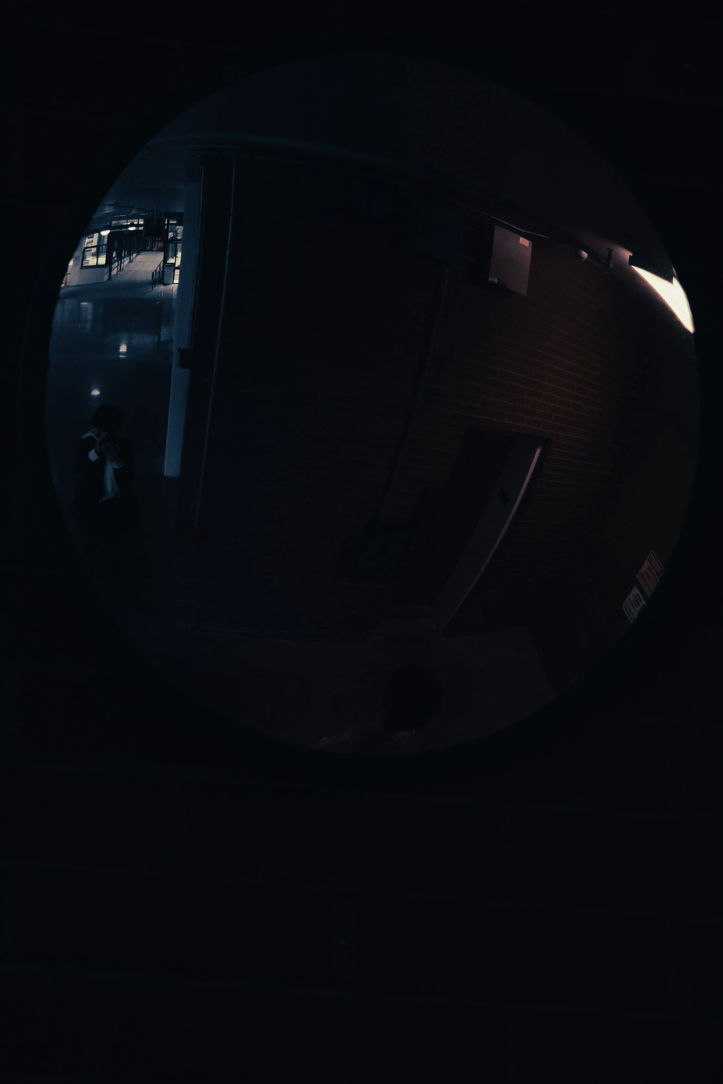 Reflection in a circular mirror showing a person taking a photo, with a corridor and glass windows in the background.