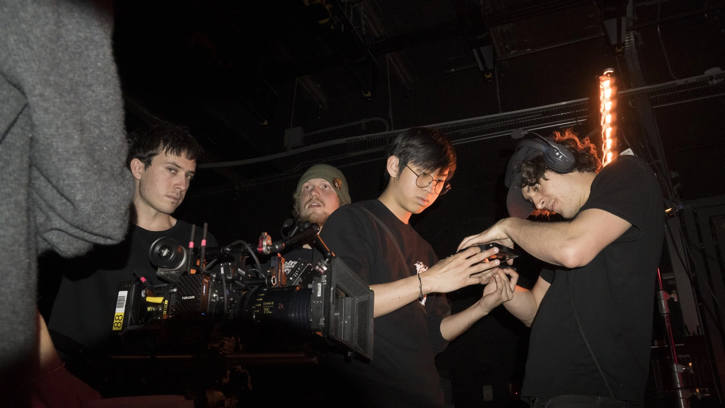 Group of four young men on a film or video set, with professional equipment, dark background, and red lighting