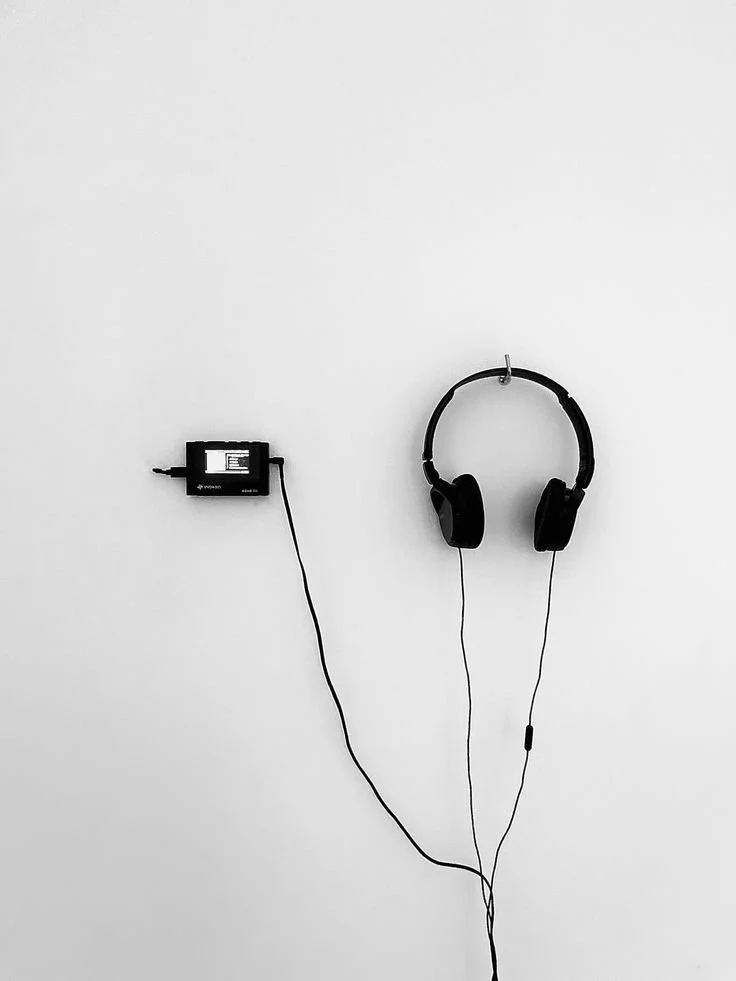 Black headphones hanging alone on a white wall, evoking listening, attention, and pause.
