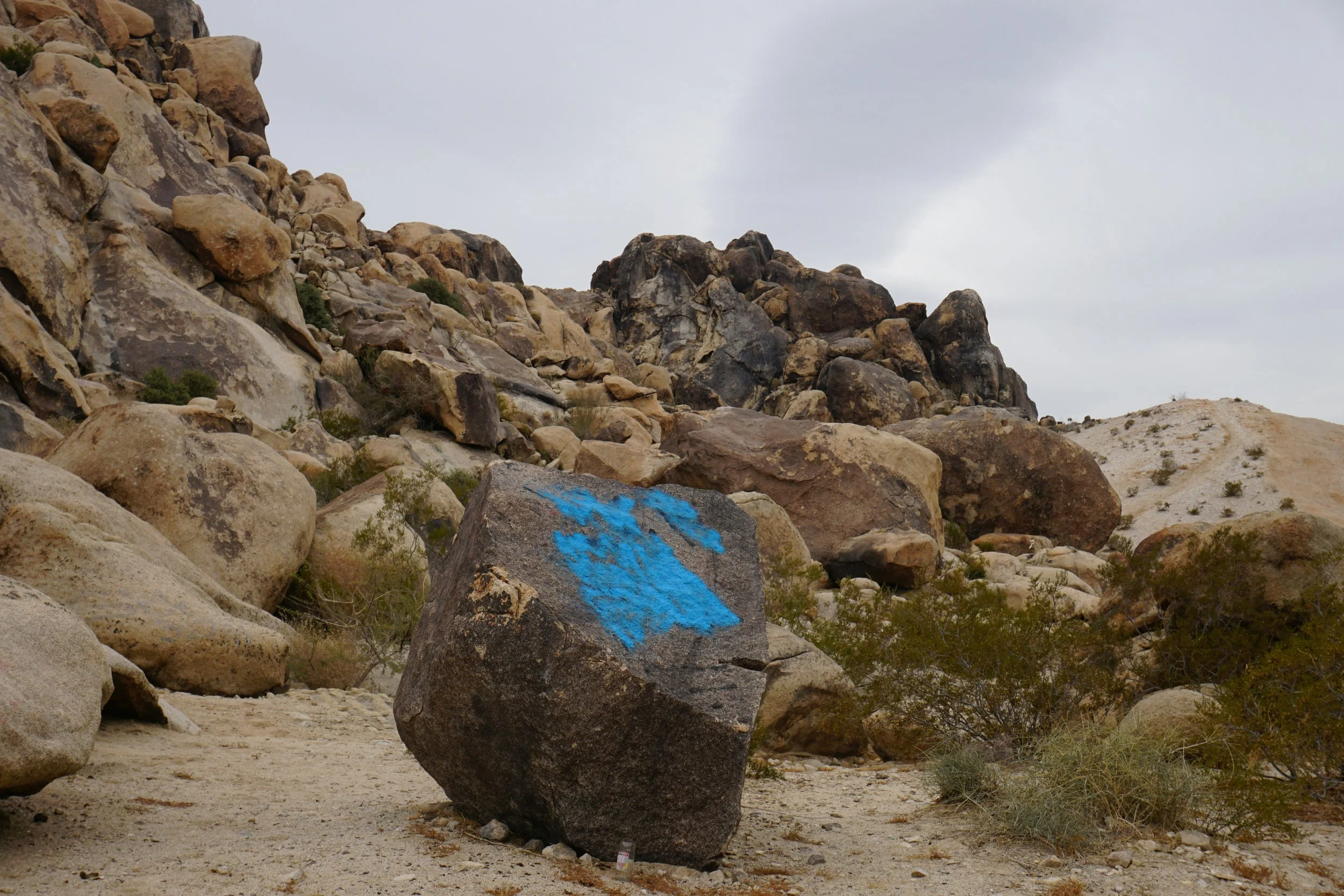 Blue arrow painted on a boulder in a rocky landscape, pointing toward an uncertain route.
