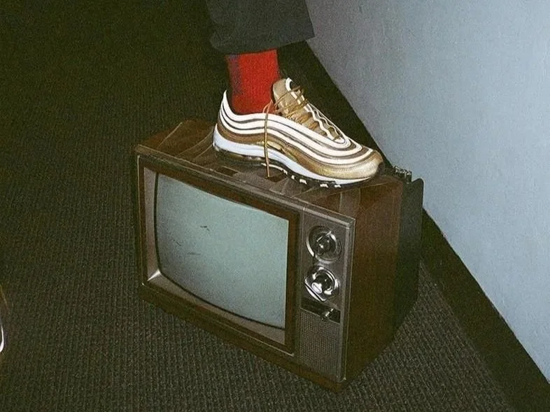 A vintage television with a person's foot wearing a sneaker and red sock resting on top of it.