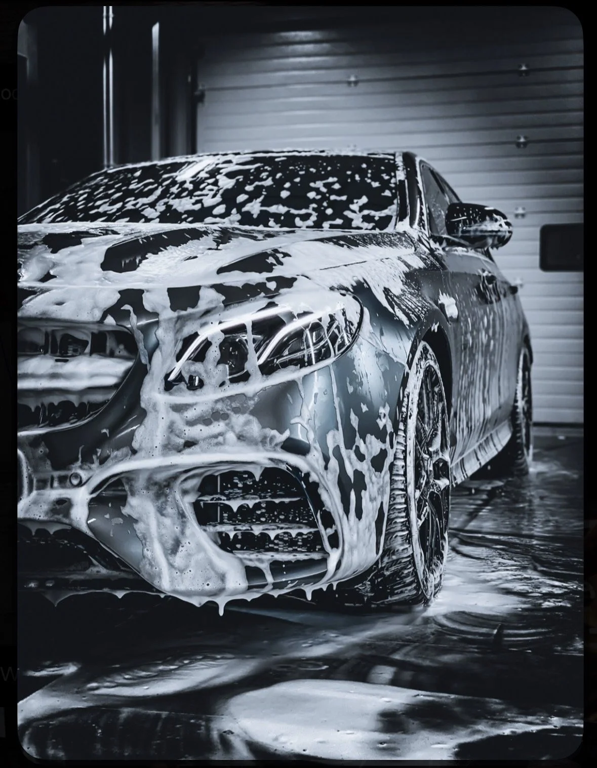A black luxury sedan car being washed with foam and soap in a garage.