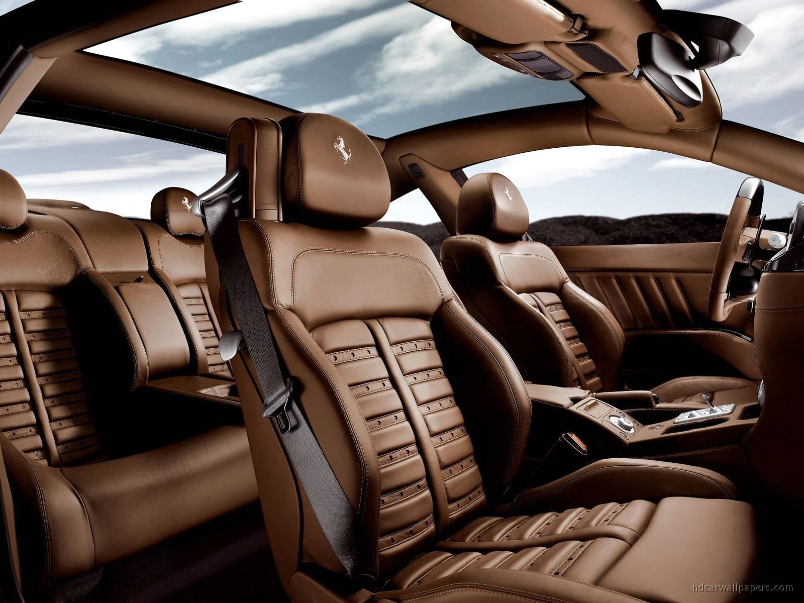 Interior of a luxury car with tan leather seats, including rear and front seats, and a panoramic sunroof showing a cloudy sky.