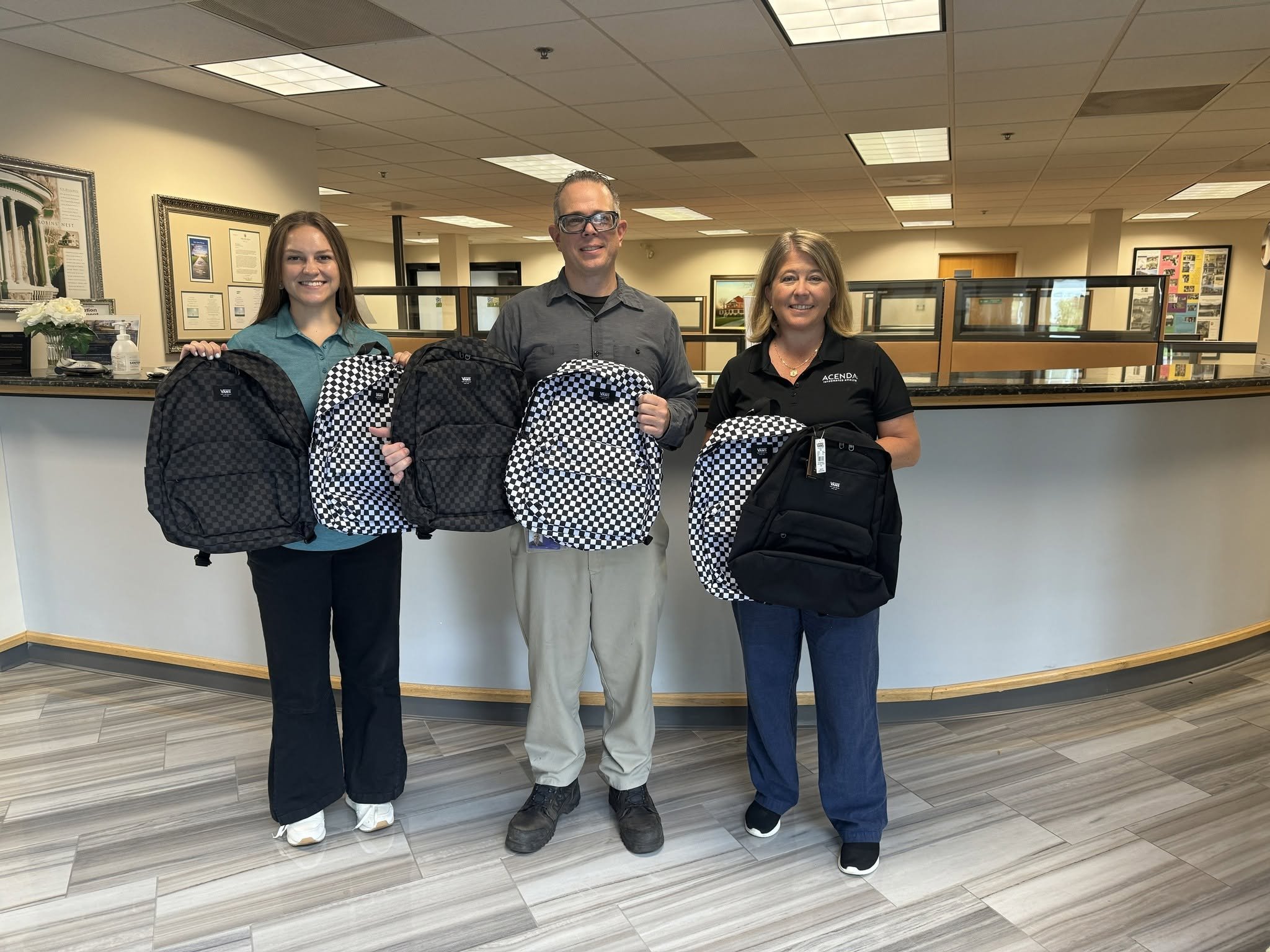Donors pose with black and checkered backpacks for Acenda's annual backpack drive