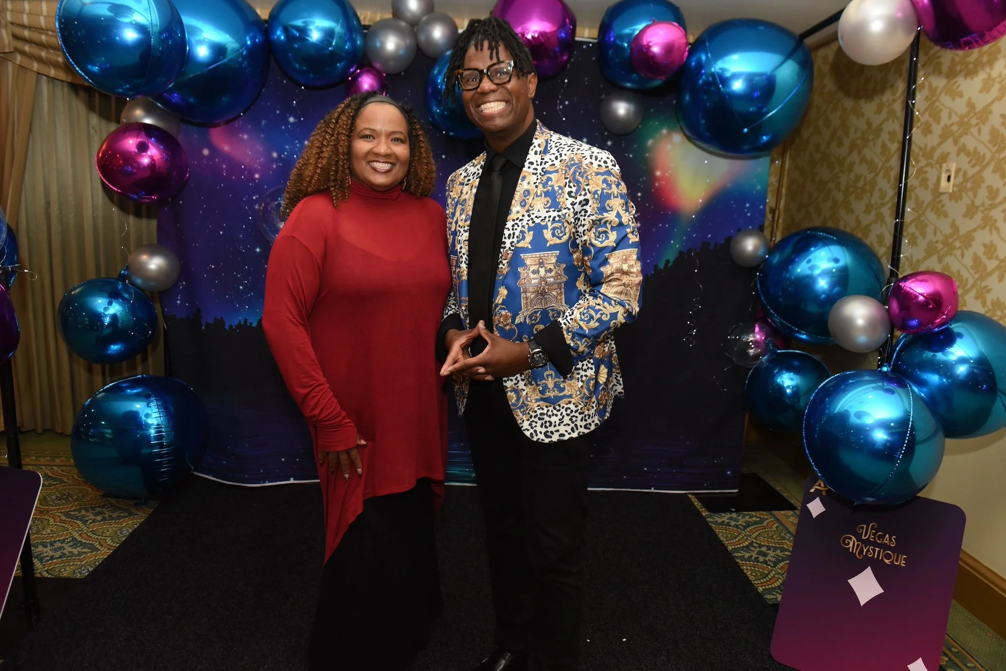 Acenda COO, Melissa Fox, poses with magician Jay Siegan at Acenda's Vegas Mystique fundraiser in front of a northern lights inspired backdrop and 3D balloon display