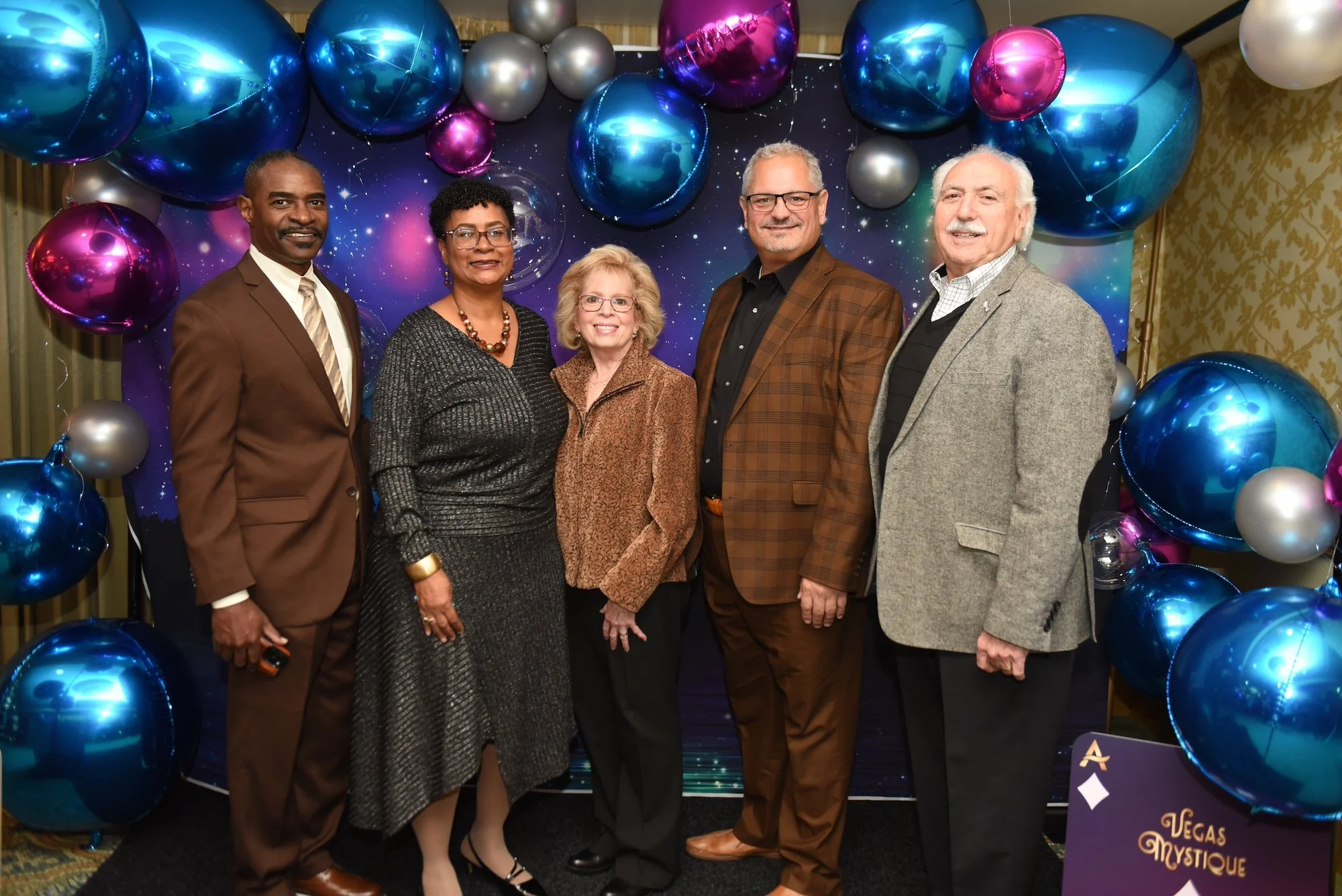 five guests pose for a photo at Acenda's Vegas Mystique fundraiser in front of a northern lights backdrop and 3D balloon display