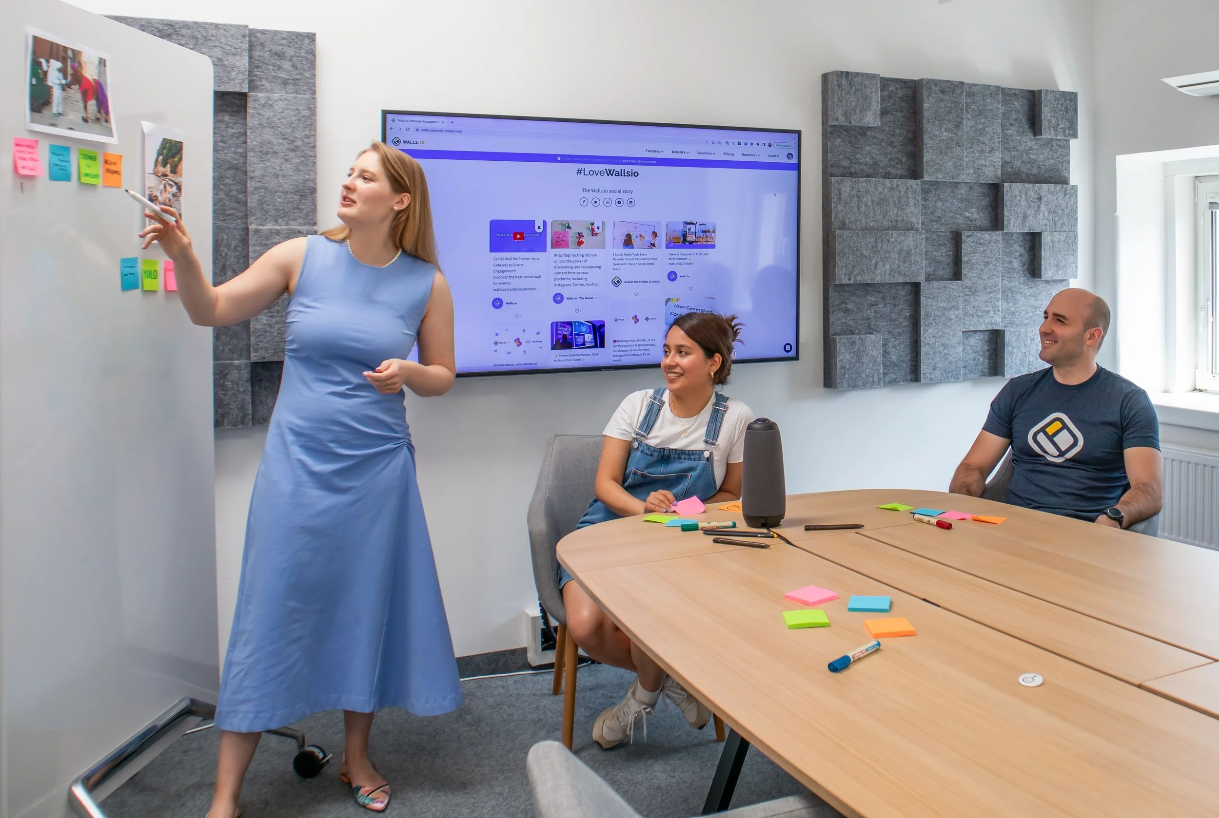 group of three coworkers brainstorming ideas in a meeting space with a white board and touchscreen tv