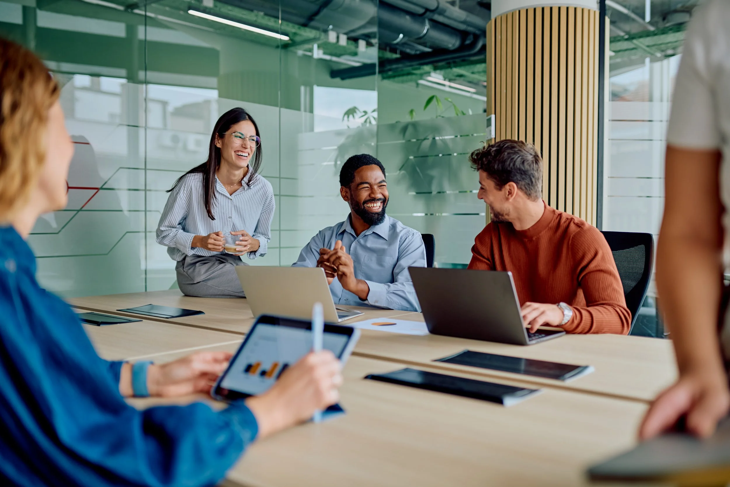 Diverse business professionals sharing ideas, smiling, and using technology during a productive meeting in a modern office environment