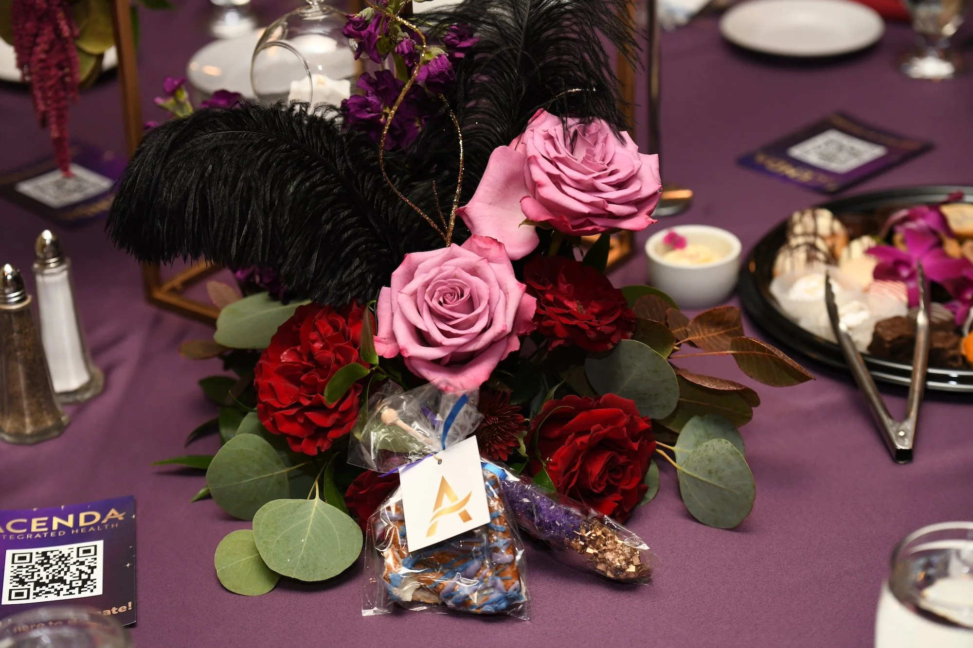 table decor featuring pink and red roses, large black feathers, gold accents, and acenda branded treats