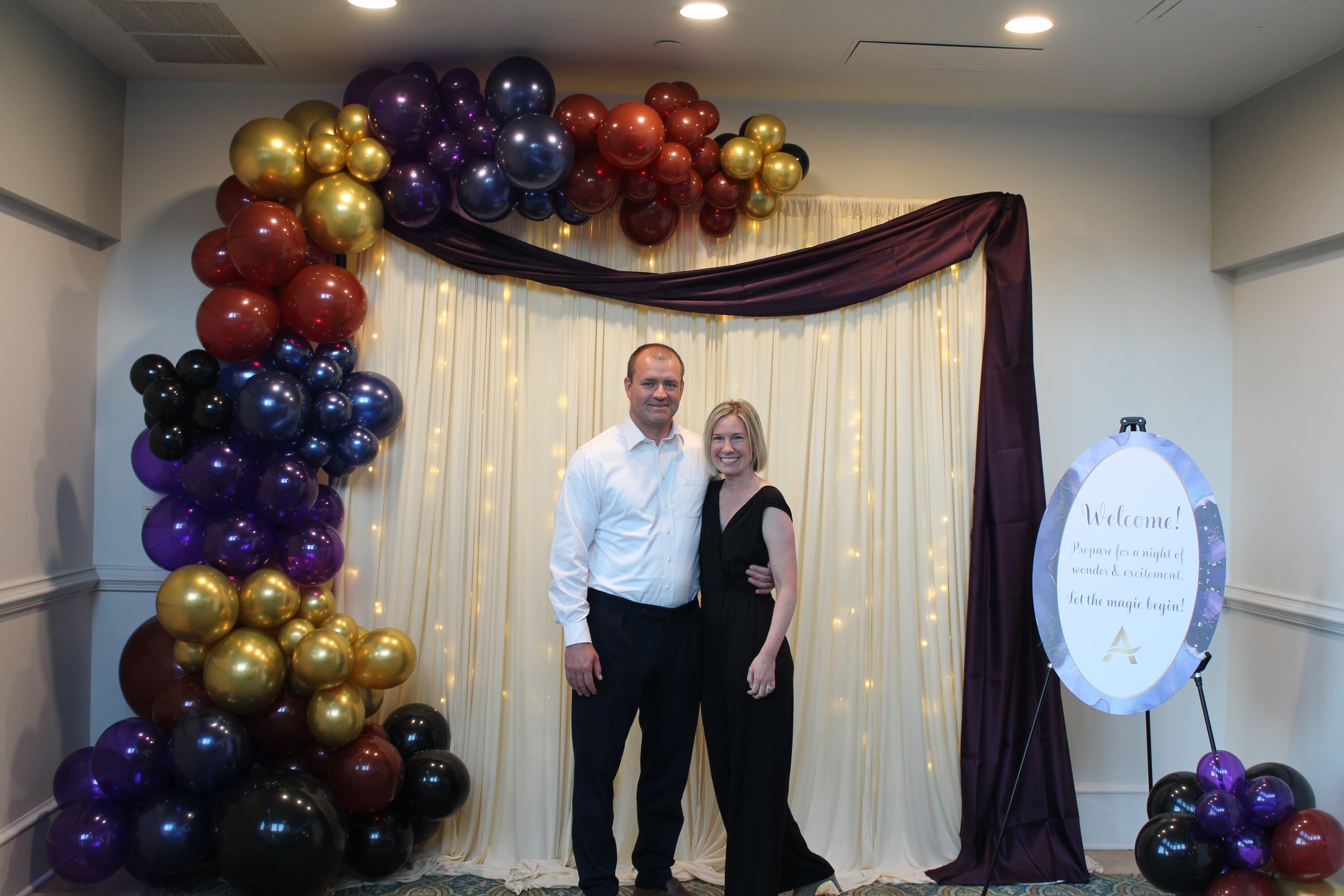 couple poses at Acenda's fall fundraiser Le Cirque in 2024 featuring a themed backdrop and balloon arch