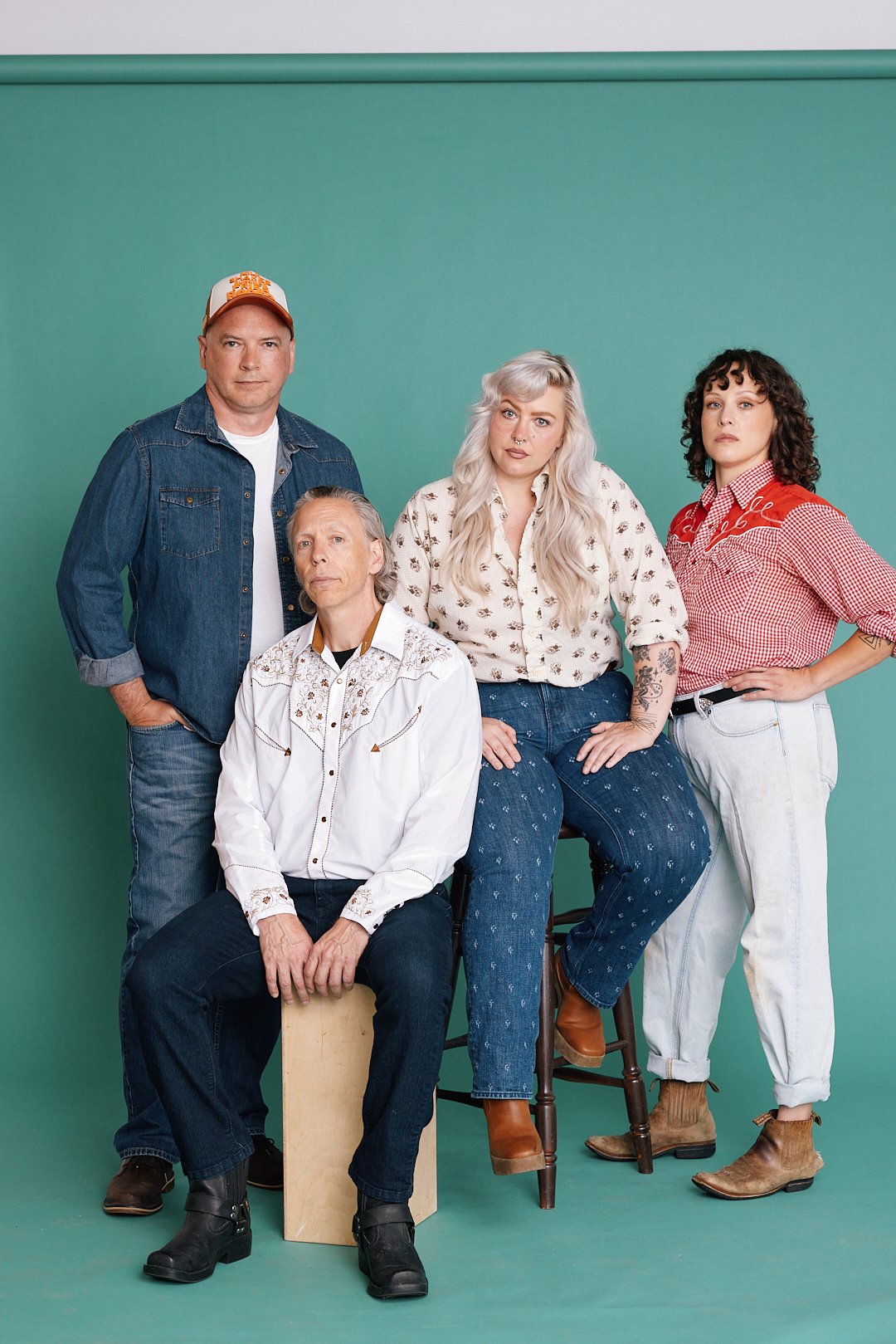 Group of five people posing against a teal background, with three standing and two sitting, dressed in casual Western-style clothing.