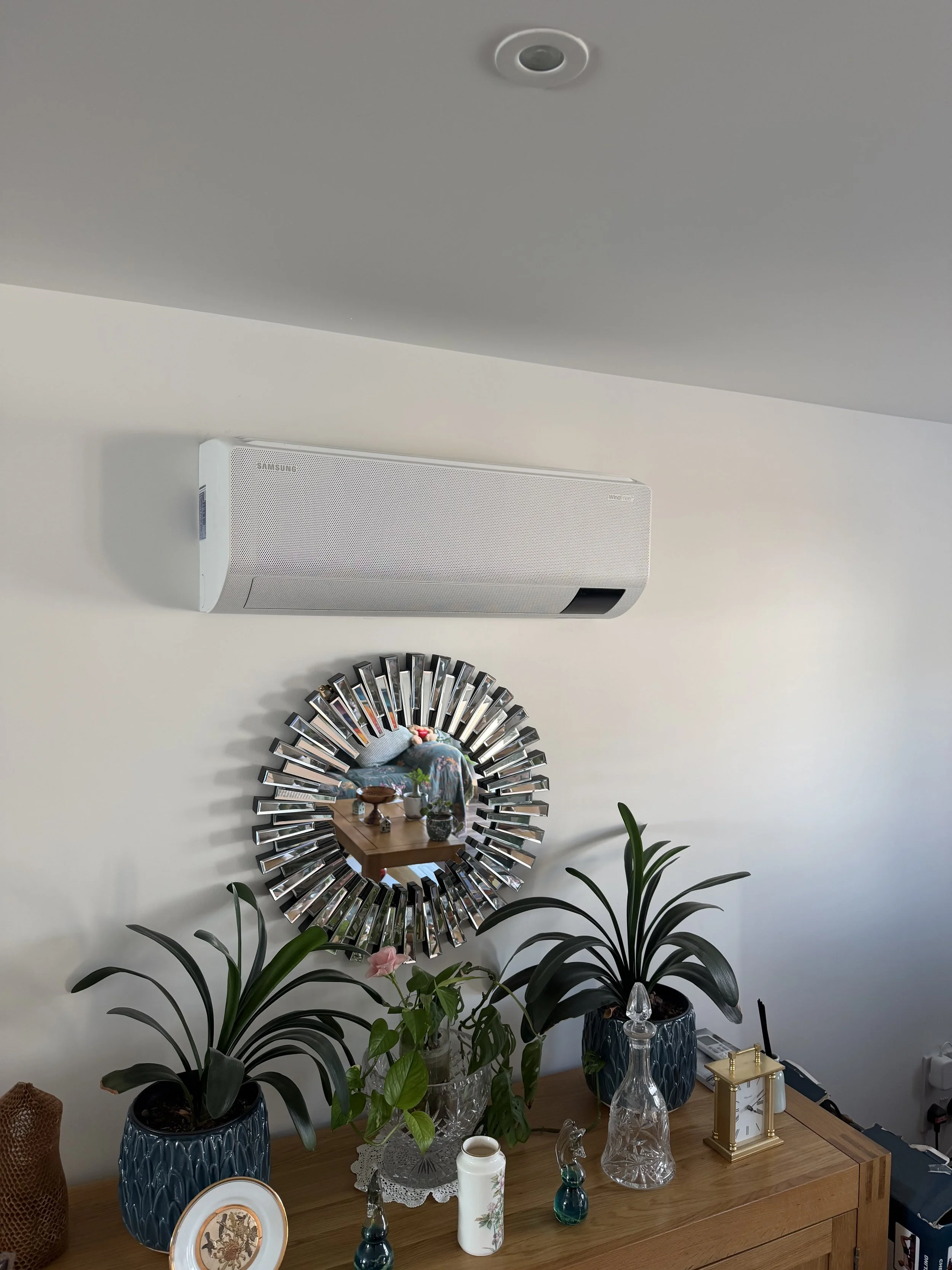 Wall-mounted air conditioning unit installed above a mirror in a modern living room.
