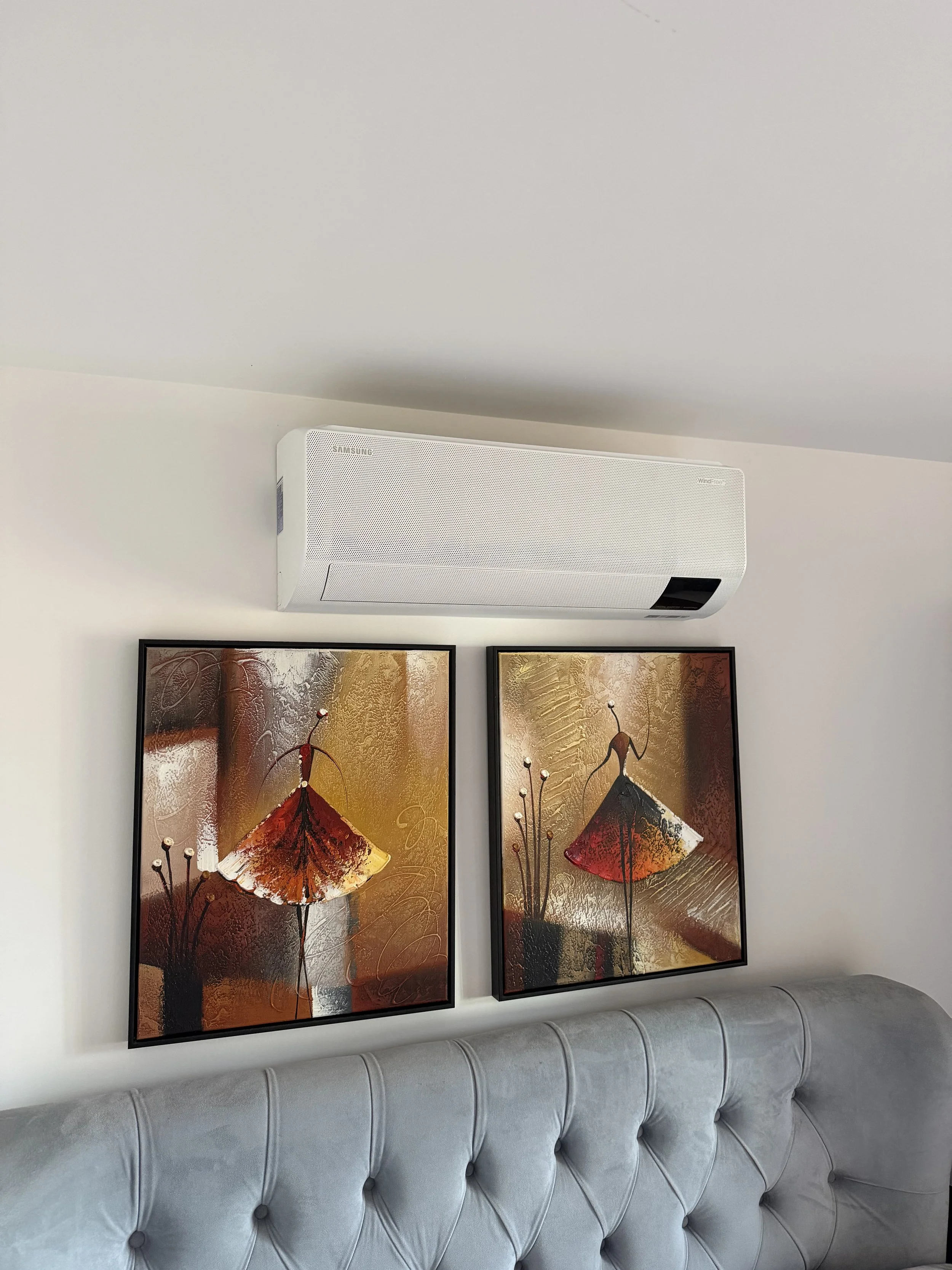 Decorative wall art featuring two panels with abstract representations of flowers or insects in warm tones of reds, golds, and browns, framed and hung above a light gray tufted sofa.