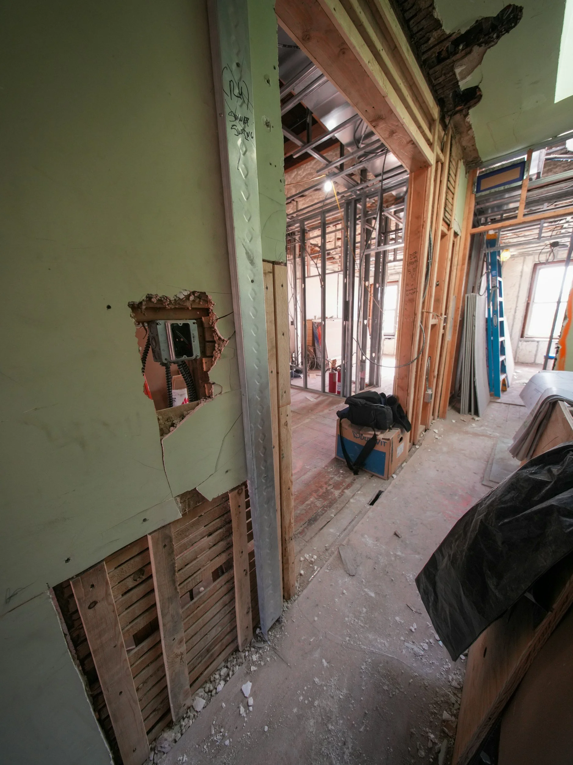 Construction site showing an interior wall under renovation with exposed wooden framing, electrical wiring, and drywall in progress. Dwellling buys as-is, no repairs required to sell.