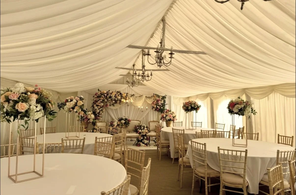Elegant wedding reception tent decorated with floral centerpieces and chandeliers.