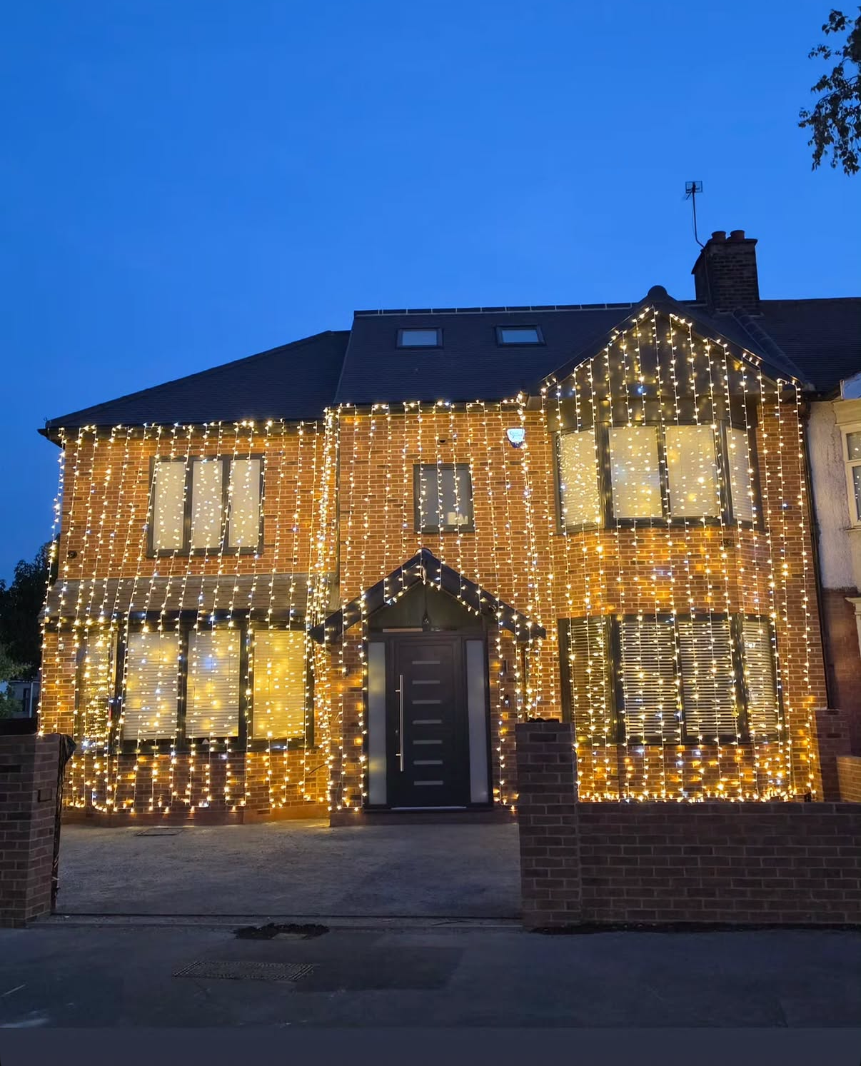 A house decorated with white and warm yellow string lights hanging from the roof and windows during the evening.
