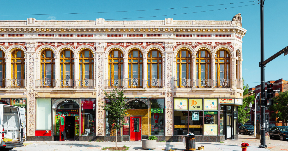 A historic building with ornate architecture housing a bookstore, groceries, and a halal restaurant, with cars parked on the street.
