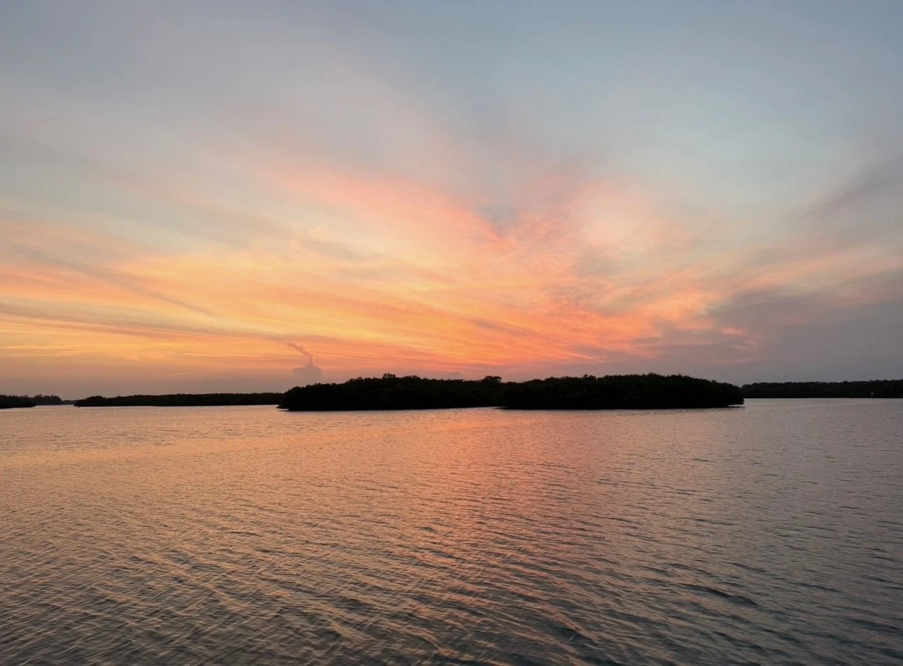 A sunset over a body of water with small islands and a pink and orange sky.