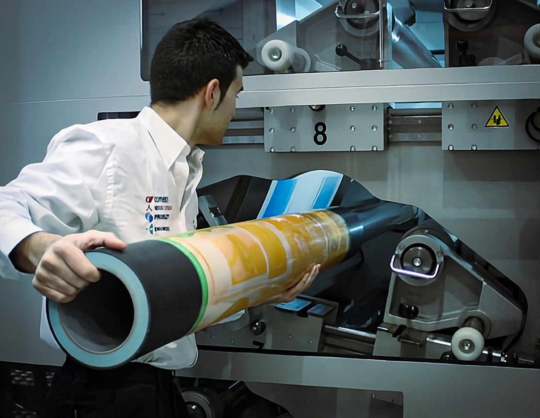 Man in white shirt inspecting a rolled-up poster in front of a machine.