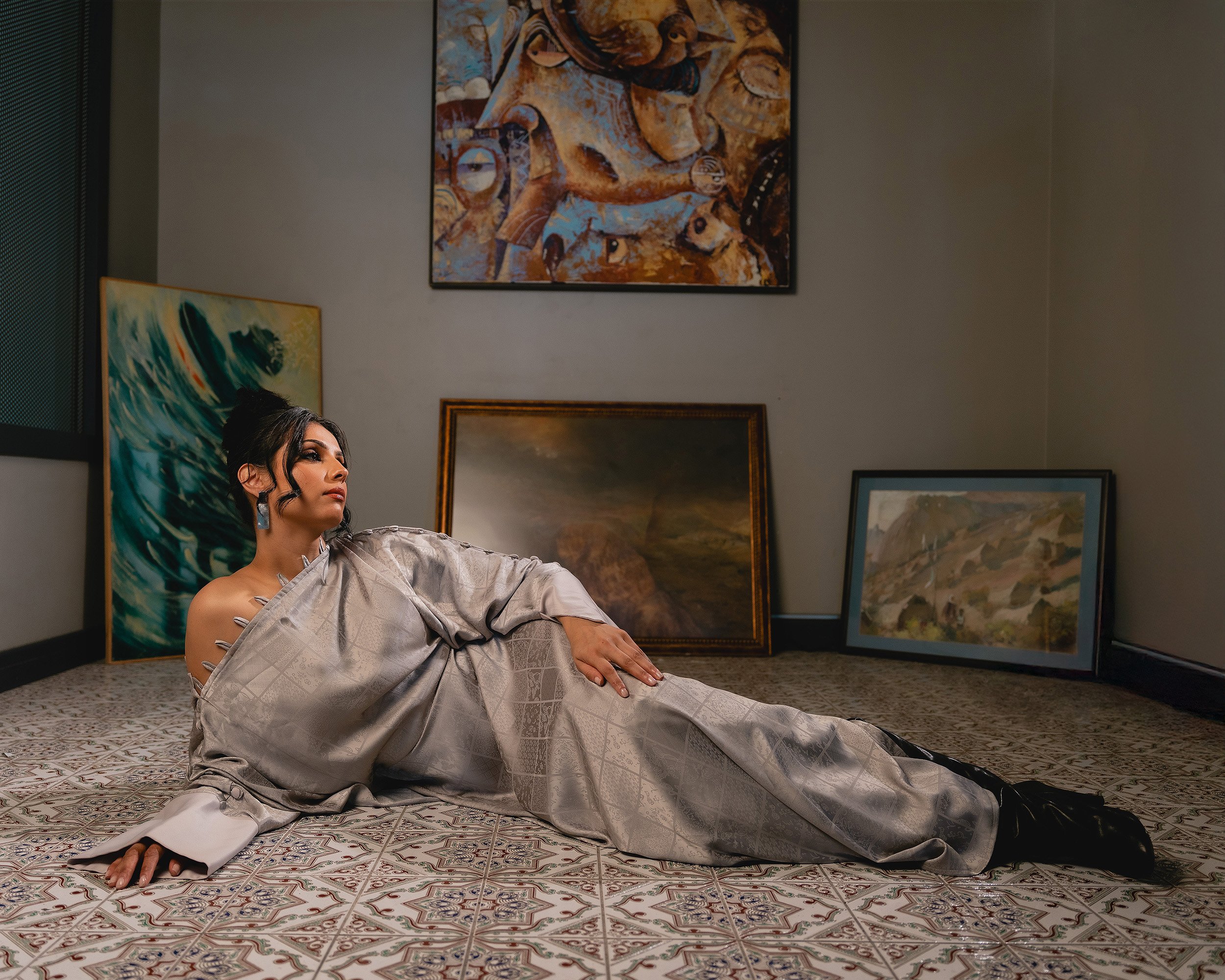 A woman in traditional attire reclining on the floor in an art gallery, surrounded by various paintings on the walls.