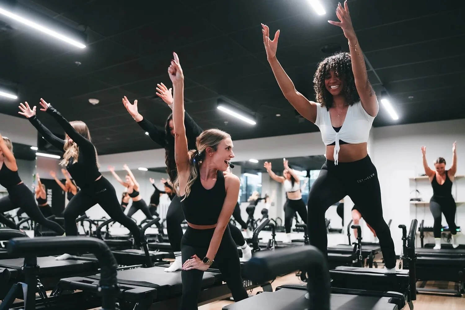 Women participating in a group fitness or dance class in a studio with exercise equipment, some wearing microphones.