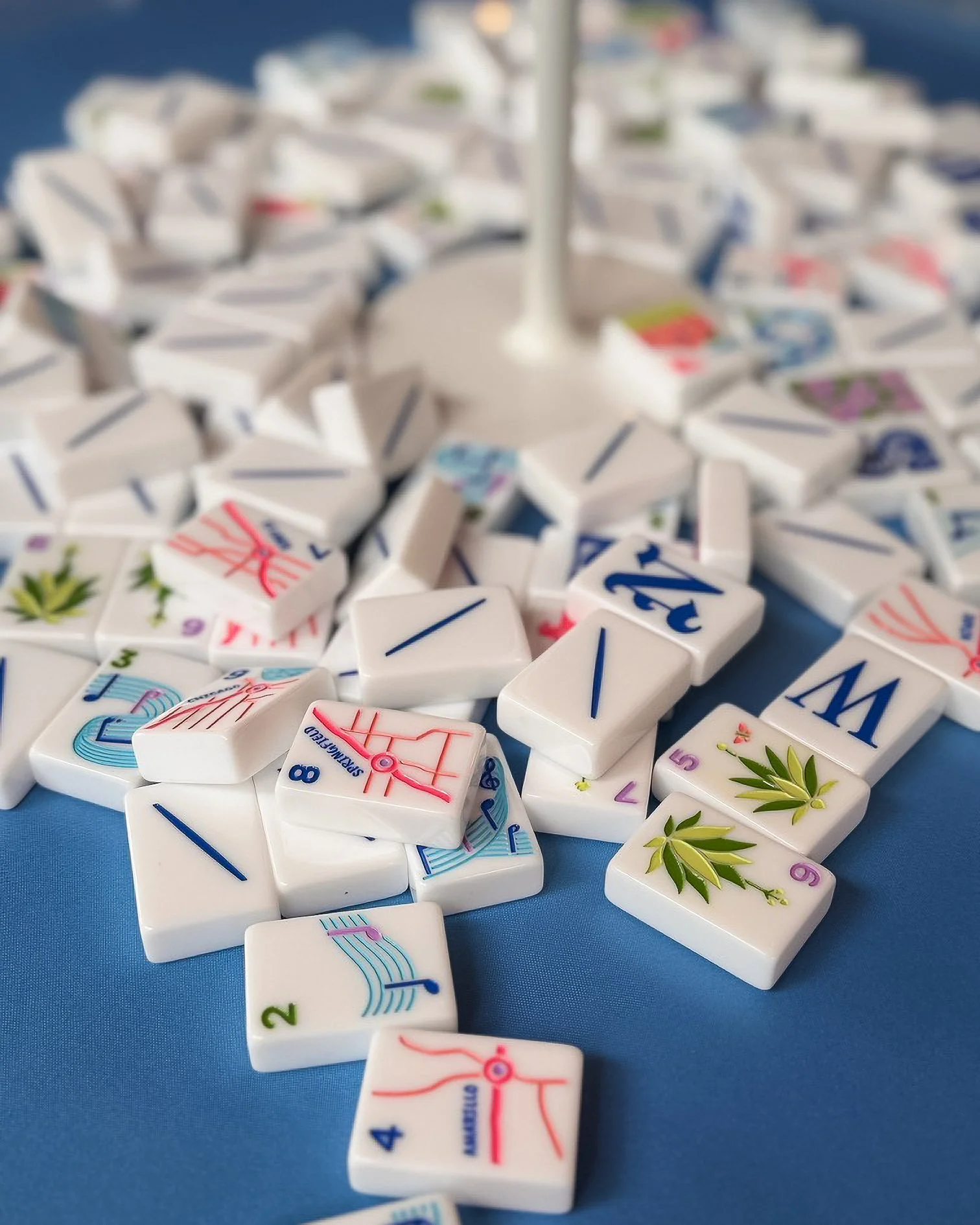 Close-up of scattered Mahjong tiles on a blue surface, some showing numbers and others with decorative designs.