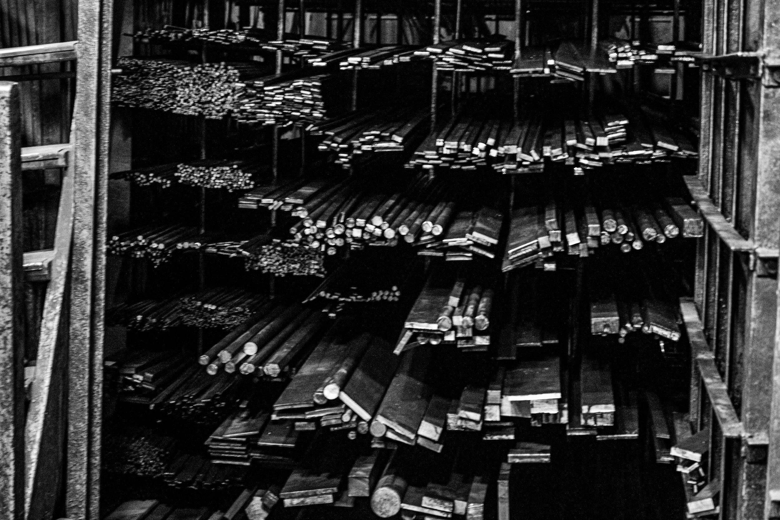 Black and white photo of shelves filled with various lengths of metal pipes stacked horizontally.