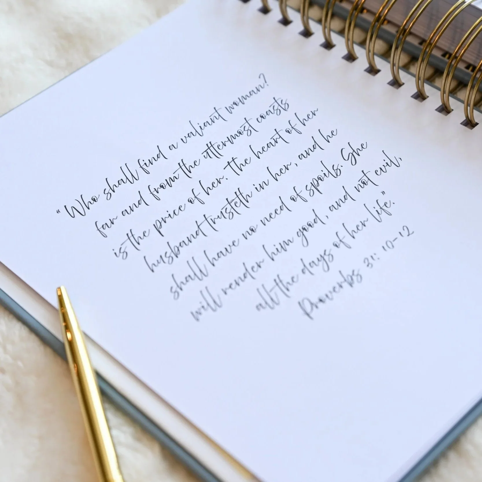 Close-up of a handwritten quote in cursive script on white paper with a gold pen resting on the paper. The quote is from the Bible.