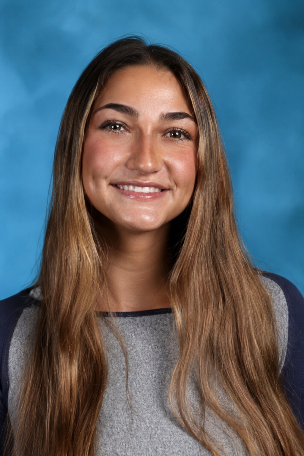 Portrait of a young woman with long, light brown hair, smiling, against a blue background.