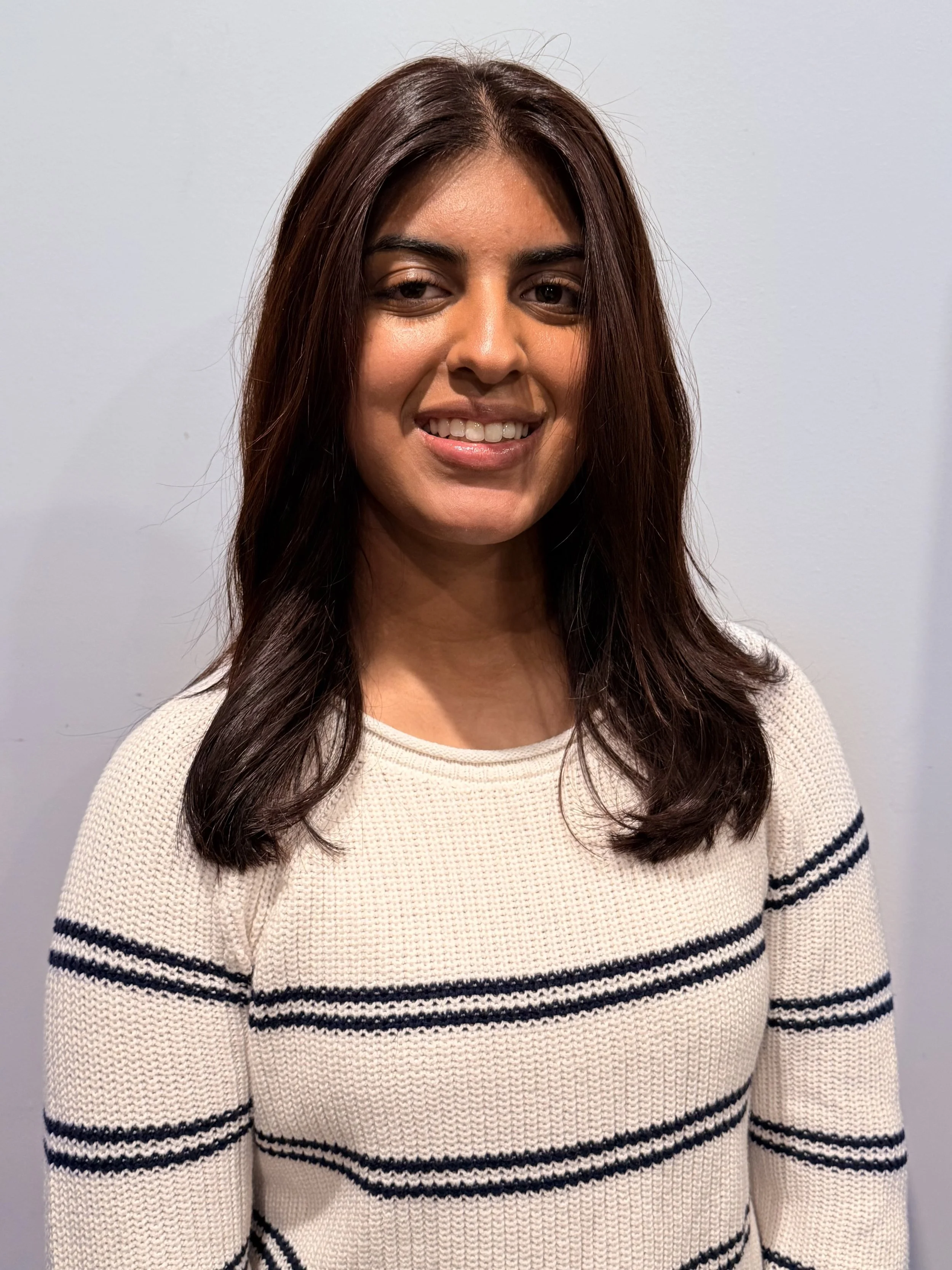 A woman with long, dark brown hair wearing a cream-colored sweater with black horizontal stripes.