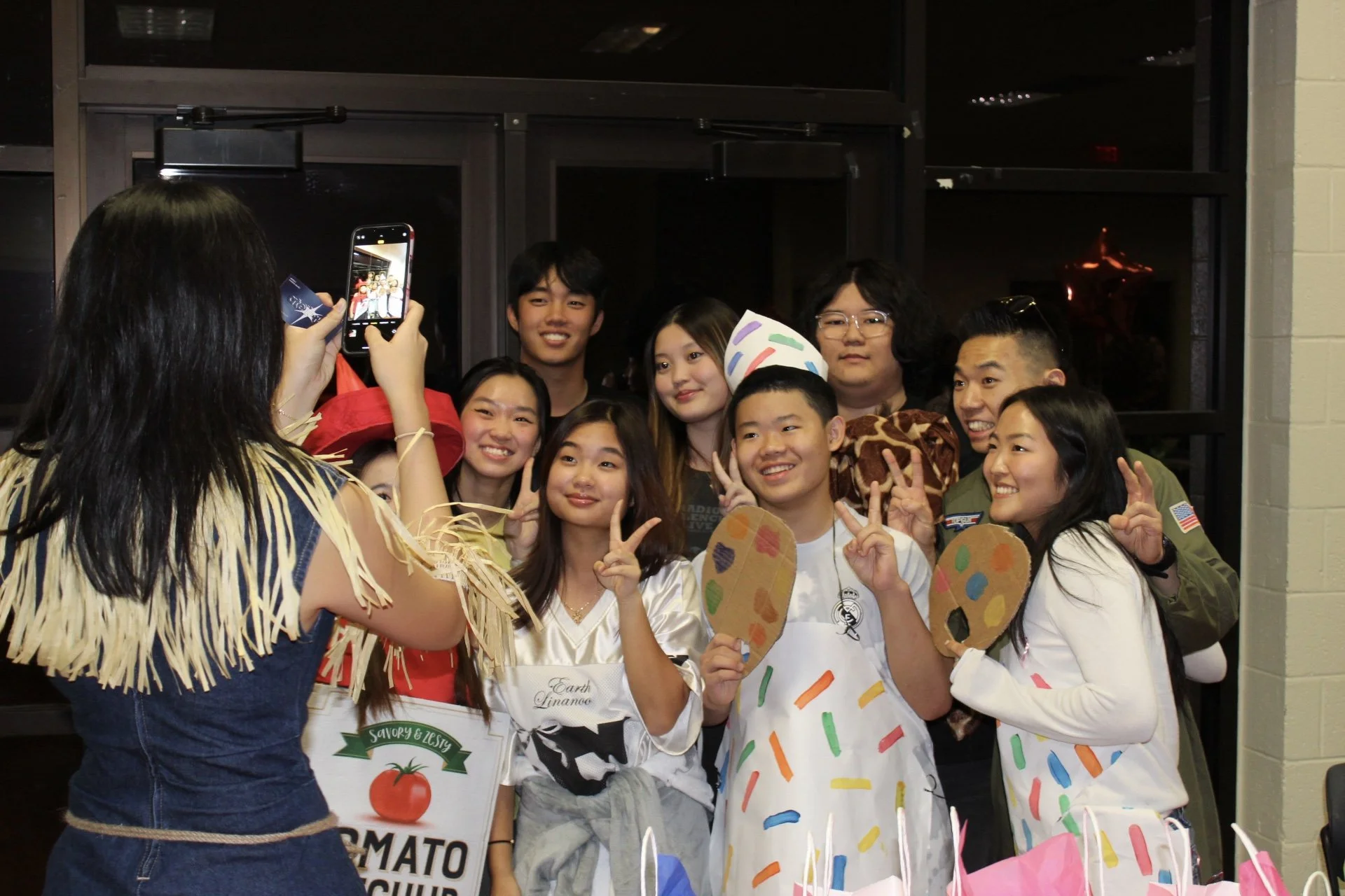 Group of children and teens taking a group photo at a celebration or event, with some children holding colorful painted paper palettes.