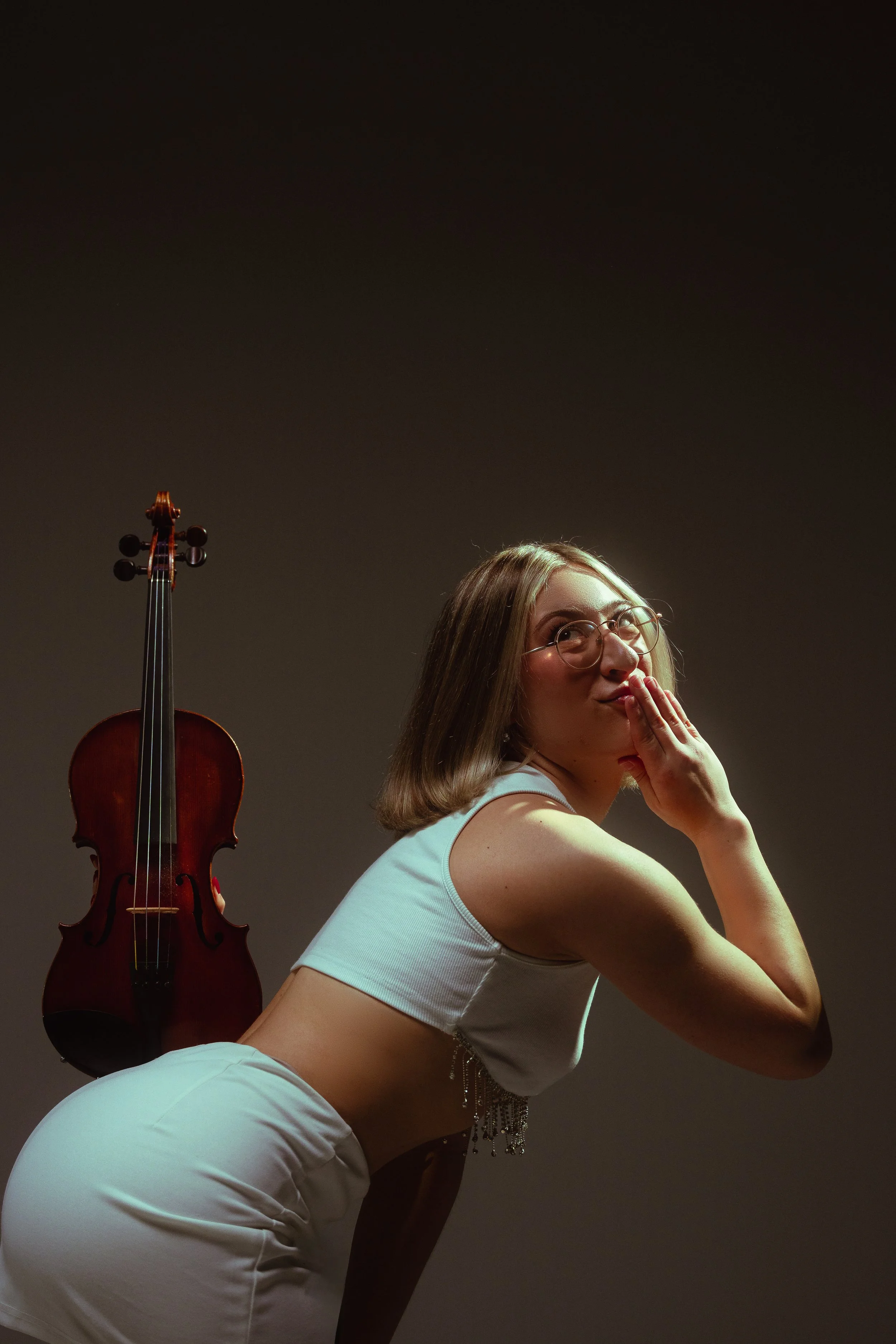 Marianne Paquin pose avec un violon sur son dos, vêtue de blanc, fond brun.