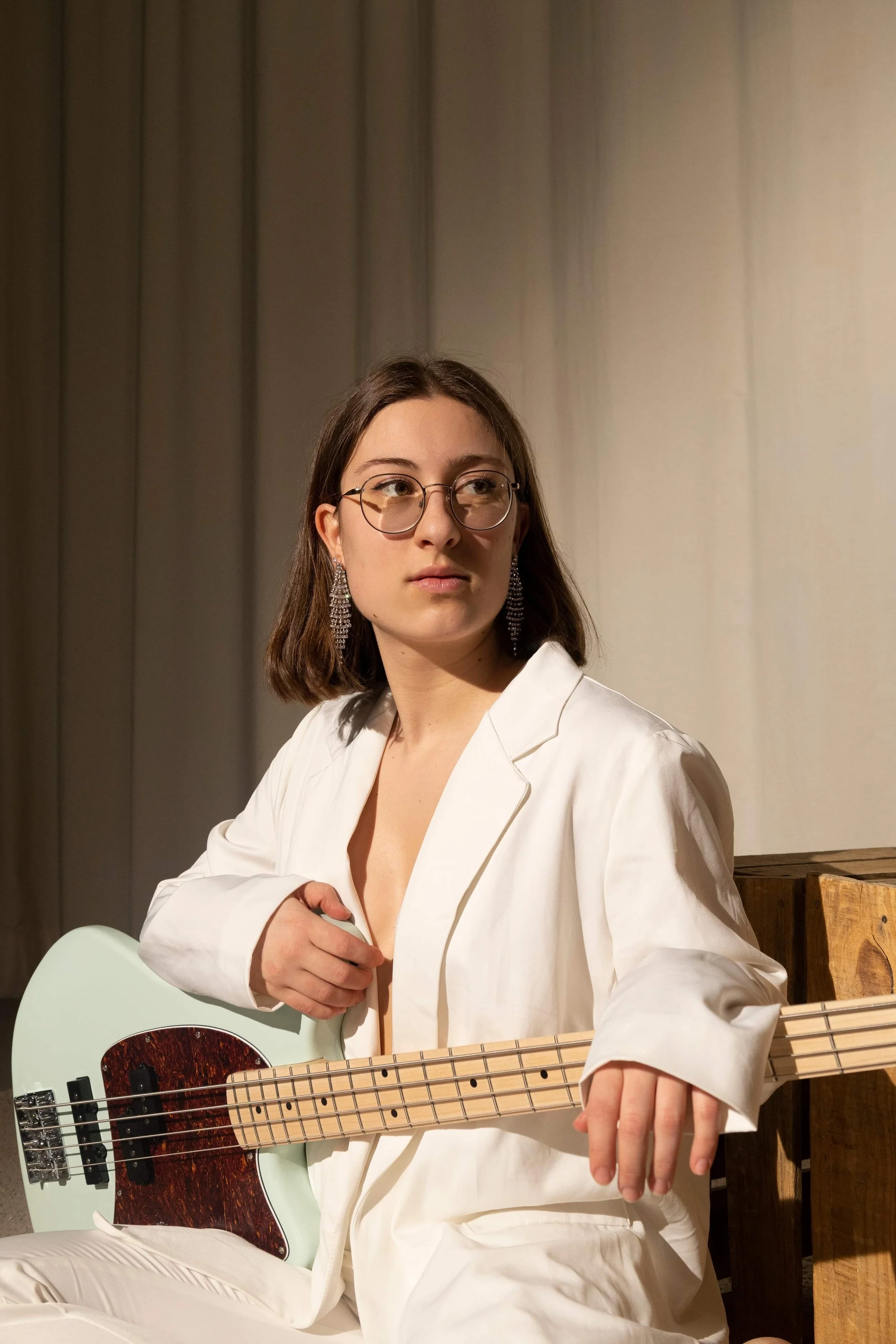 Marianne Paquin avec une basse électrique, porte une blouse blanche, sur fond brun.
